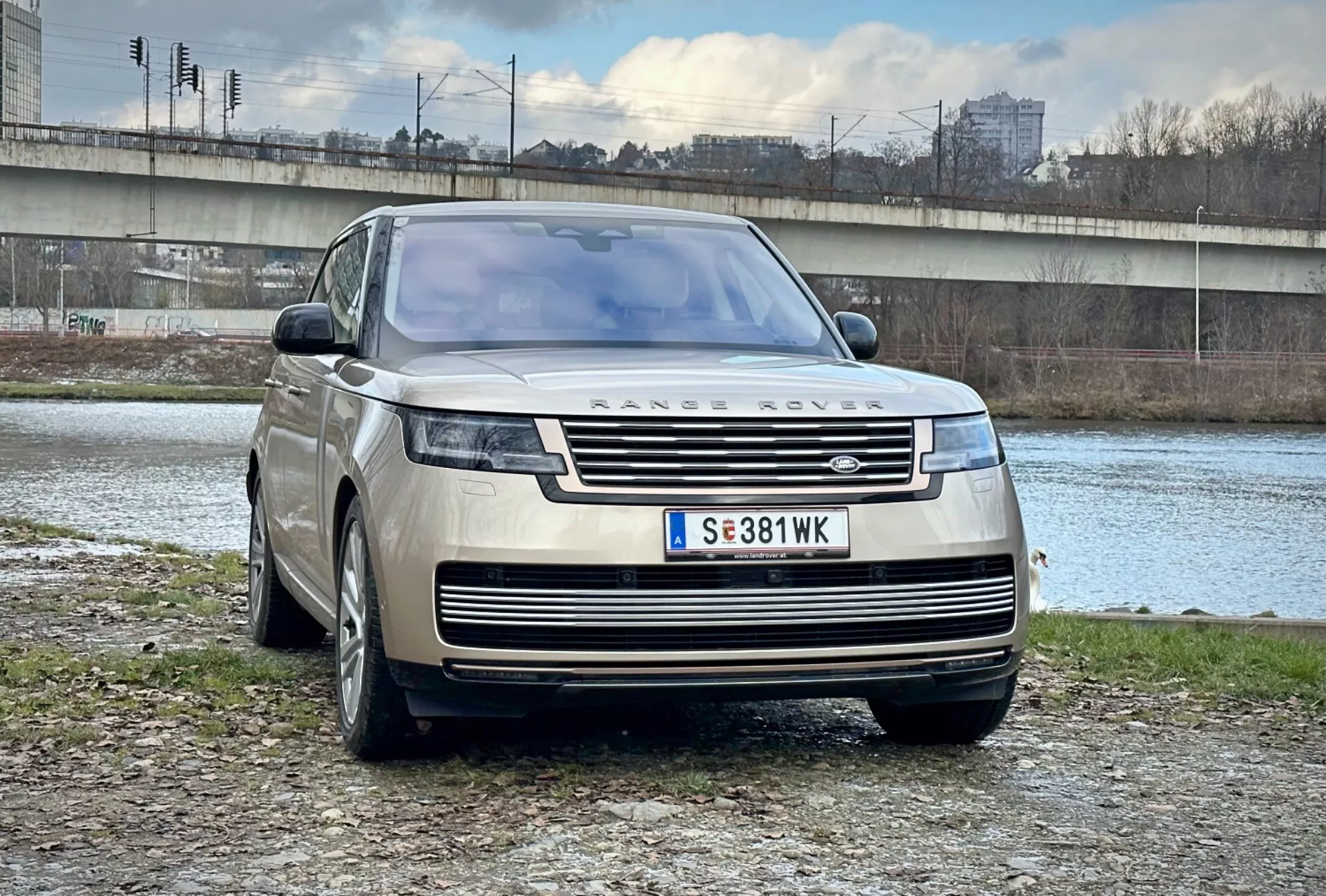 SUV de luxe Range Rover 2021 garé en extérieur près d'une rivière et d'un pont dans un cadre urbain, présentant son design moderne, sa grille avant et ses phares LED élégants