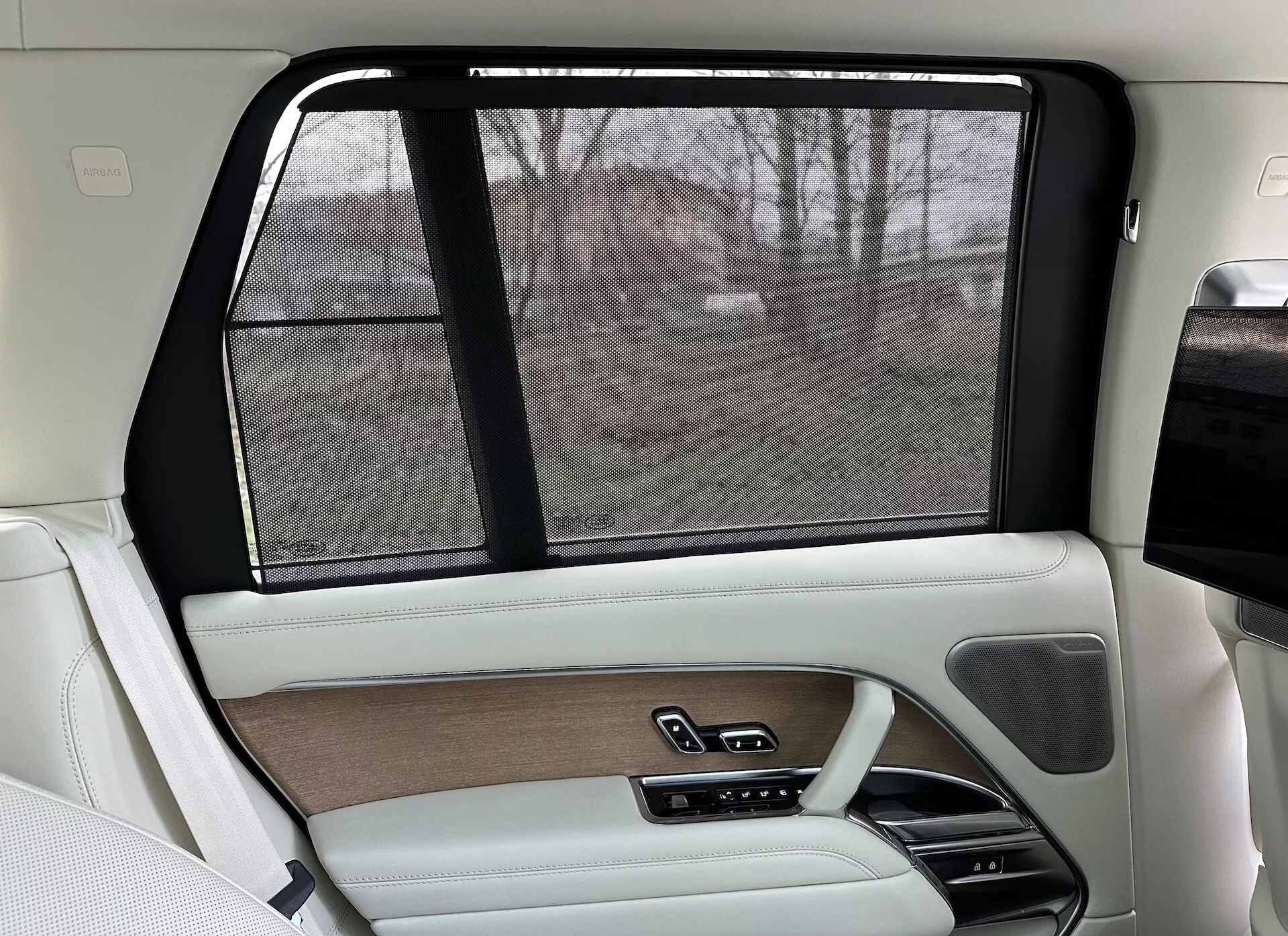 Intérieur côté passager arrière d'un Land Rover Range Rover 2021, présentant un design luxueux beige et noir, garnitures en bois, finitions en cuir, pare-soleil électronique et systèmes de contrôle avancés