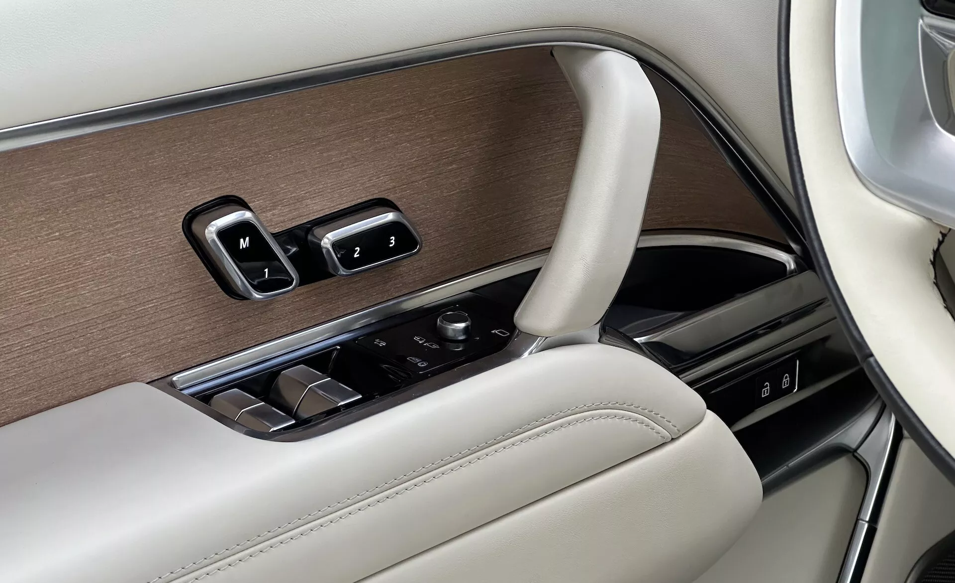Détail intérieur du Land Rover Range Rover 2021 montrant le panneau de porte côté conducteur avec contrôles des fenêtres, réglages des miroirs, paramètres de mémoire de siège dans un design luxueux avec finitions en bois, chrome et cuir, et un bouton de contrôle pour l'infodivertissement.