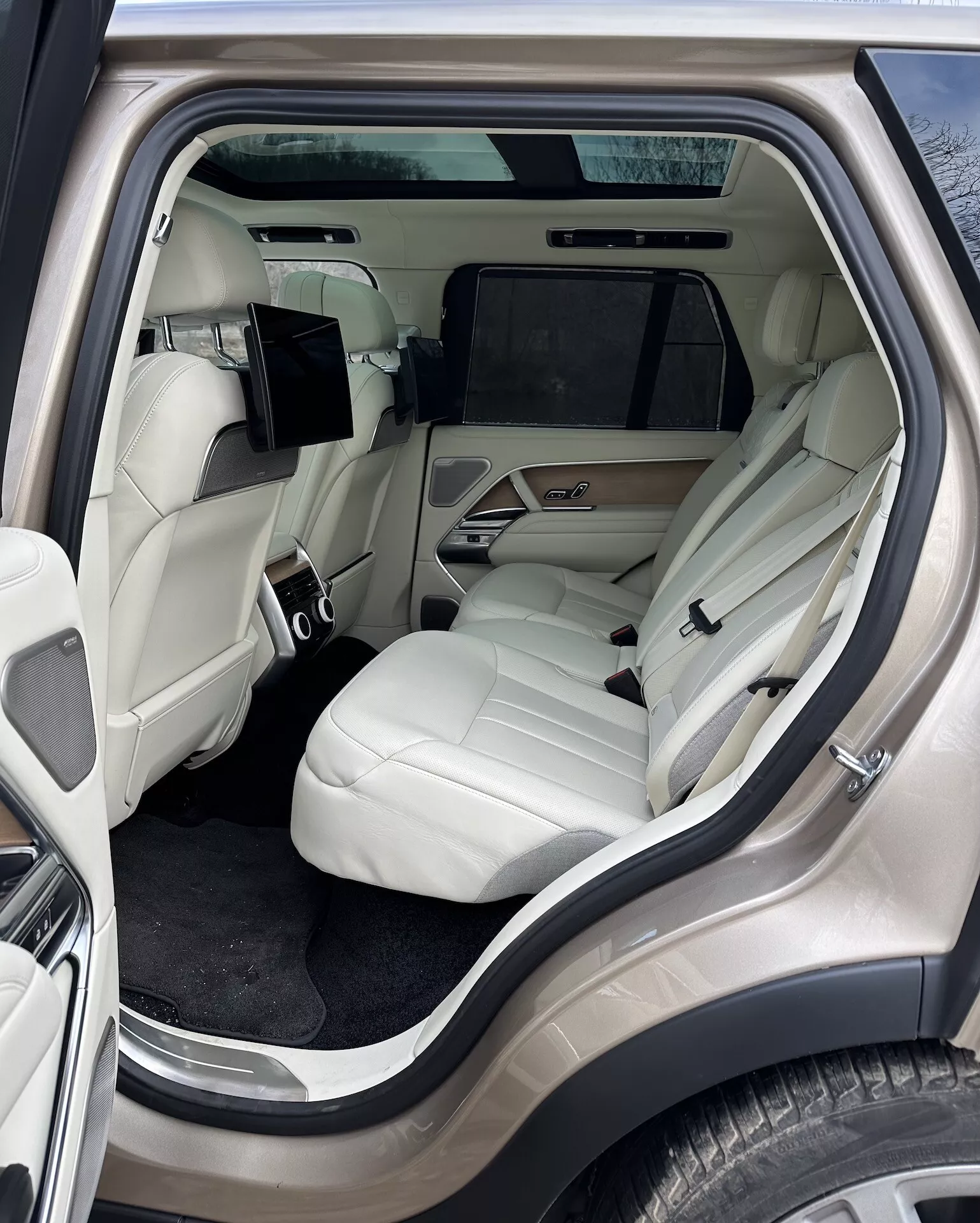 Vue intérieure du Land Rover Range Rover 2021 se concentrant sur le compartiment passagers arrière luxueux depuis un angle latéral extérieur, présentant des sièges en cuir de couleur claire, une console centrale avancée, un système de divertissement et des détails de luxe