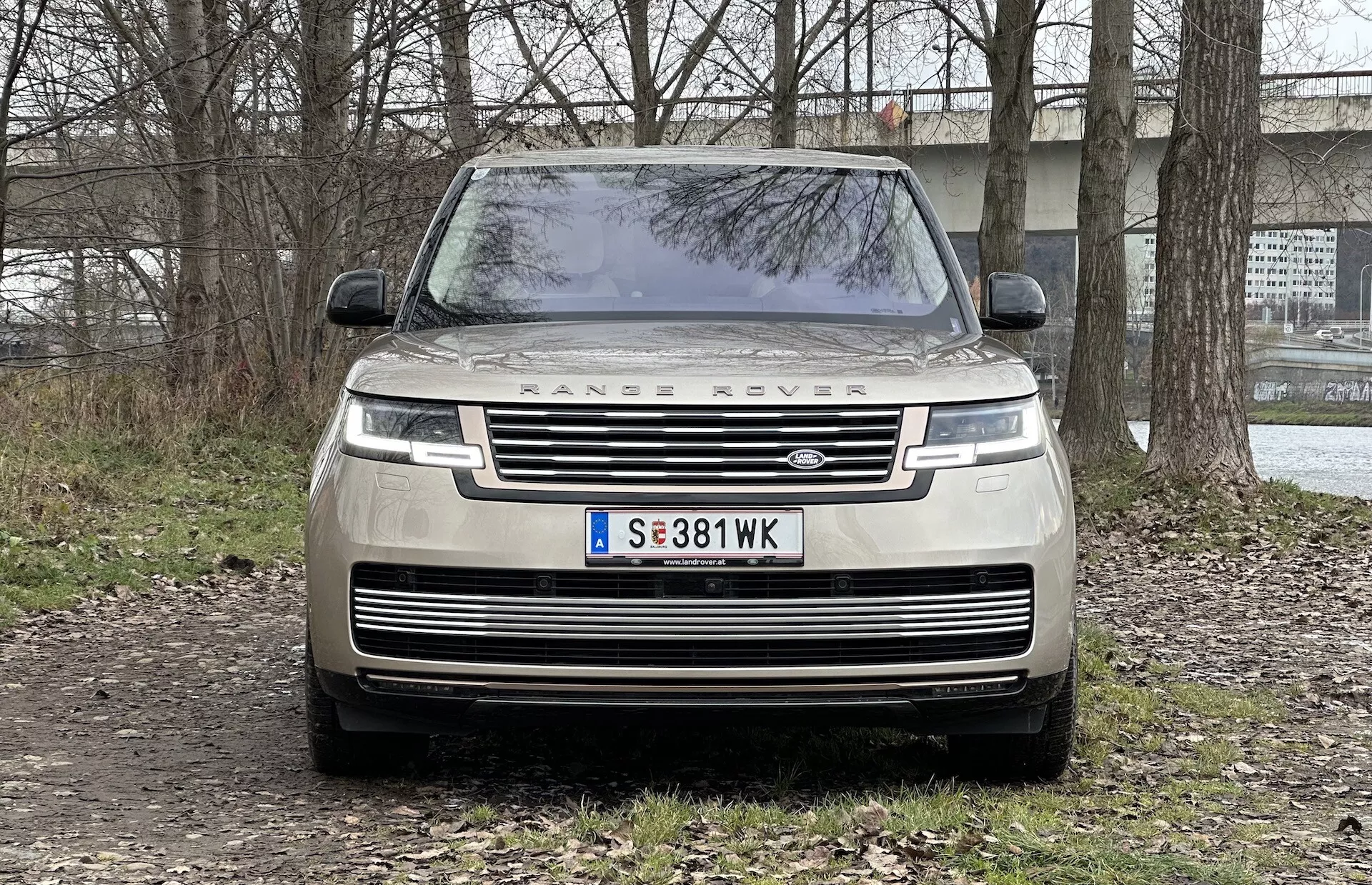 Vue de face d'un Range Rover 2021 montrant la grille, les phares LED, l'inscription 'RANGE ROVER' sur le capot, et garé sur une surface non pavée avec un arrière-plan semi-rural