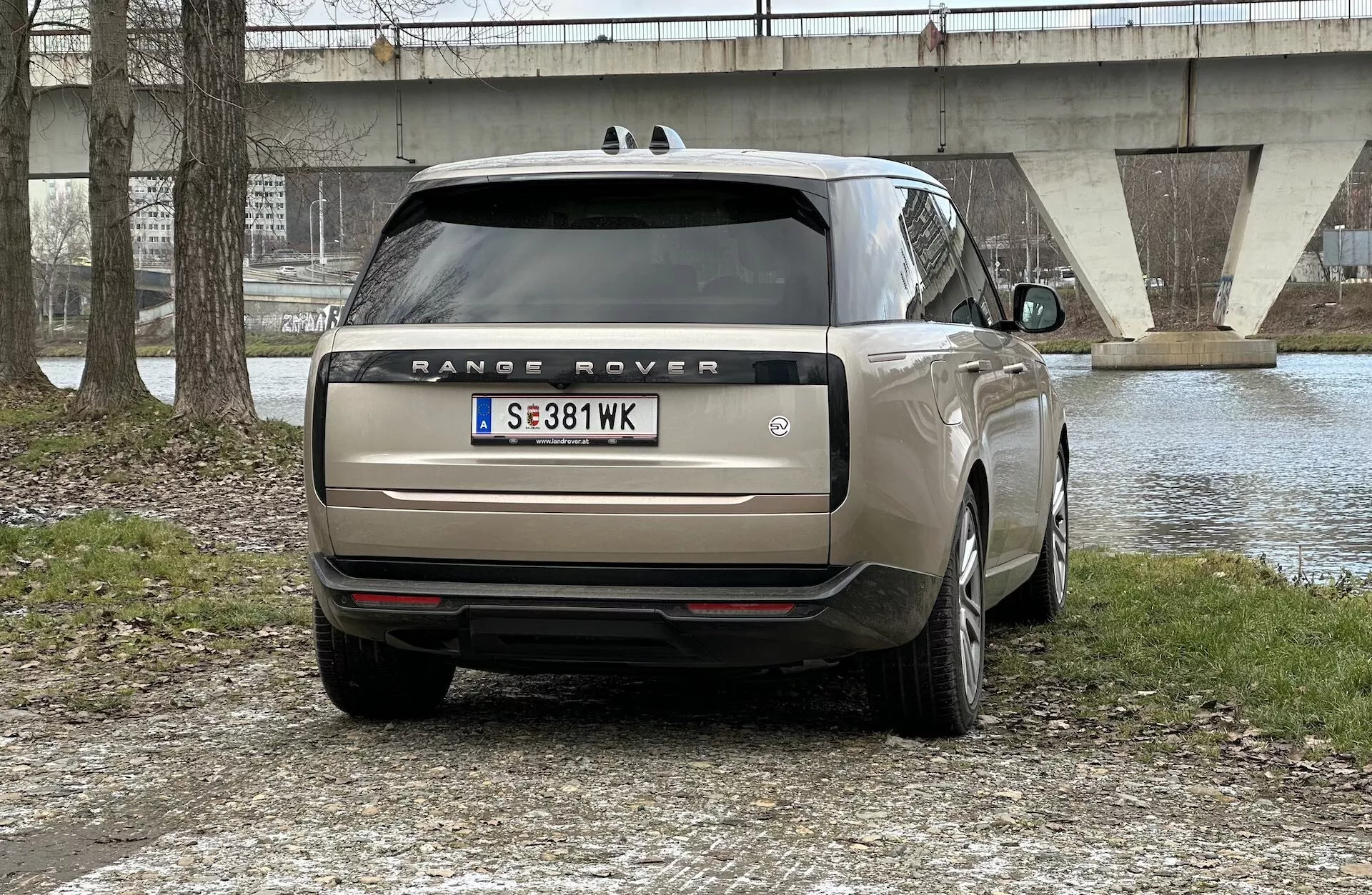 Vue arrière d'un Range Rover 2021 garé en extérieur avec un plan d'eau et un pont en arrière-plan, montrant des feux arrière LED, un double échappement, des vitres teintées et des jantes en alliage multi-branches.