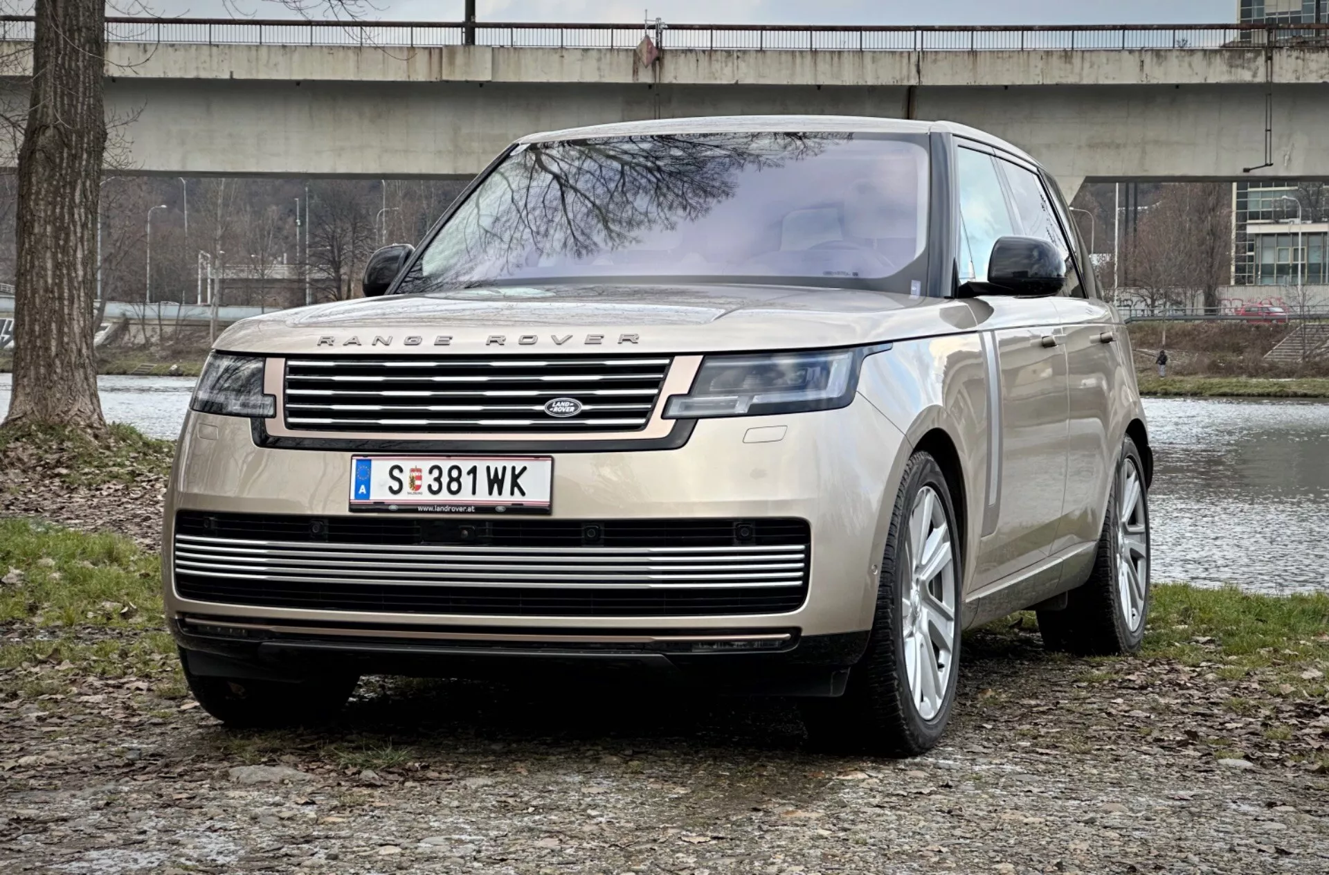 Range Rover 2021 dans une vue impressionnante à trois quarts avant montrant sa grille distinctive, ses phares avant LED élégants et sa plaque de protection avant robuste sur un fond de parc urbain, soulignant le luxe et la capacité tout-terrain.