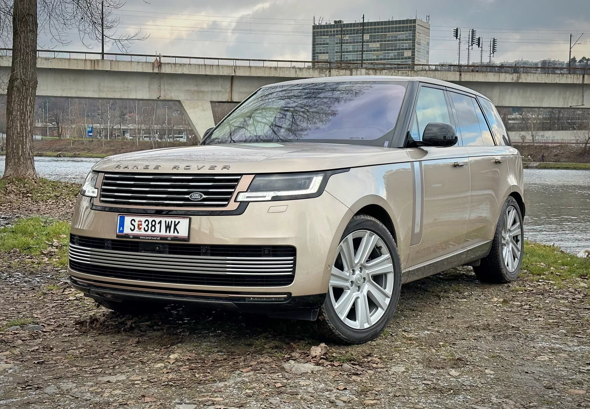 SUV de luxe Land Rover Range Rover 2021 garé sur un terrain mixte de terre et d'herbe avec une structure en béton et de la végétation en arrière-plan, montrant vue de l'angle avant mettant en évidence les phares LED, les roues en alliage et les caractéristiques aérodynamiques modernes