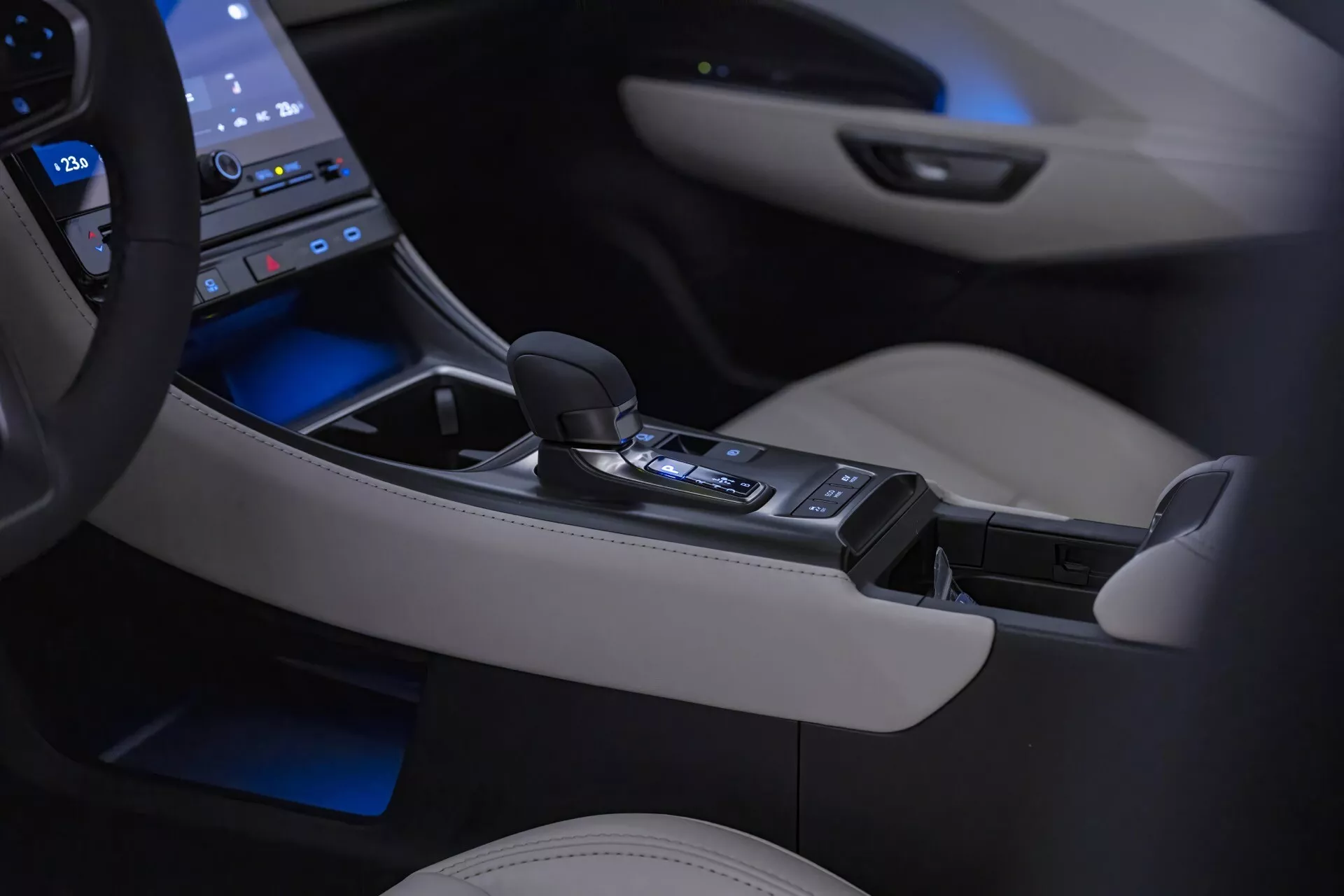 Intérieur du Lexus LBX 1ère Génération 2024 présentant la console centrale et le levier de vitesse automatique avec éclairage d'ambiance, entouré d'un panneau tactile high-tech, et des détails en cuir crème de luxe