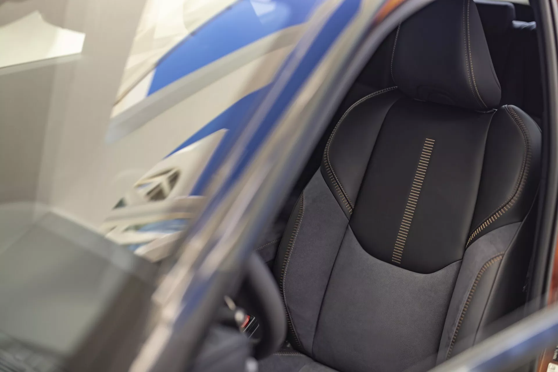 Gros plan sur le siège conducteur du Lexus LBX 1ère génération 2024 présentant une sellerie en matériau foncé de haute qualité avec couture détaillée et design de soutien latéral sportif, vue à travers une porte ouverte avec accent sur les caractéristiques ergonomiques et les commandes possibles de réglage du siège électrique.