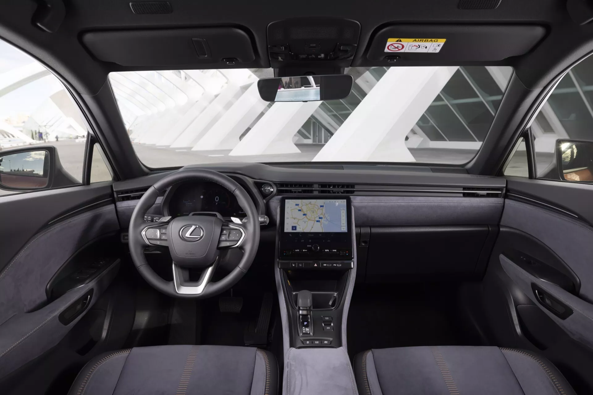 Vue intérieure du Lexus LBX 2024 montrant tableau de bord, volant avec logo Lexus et commandes intégrées, console centrale tactile, sièges de luxe, et caractéristiques technologiques avancées depuis la perspective du siège arrière