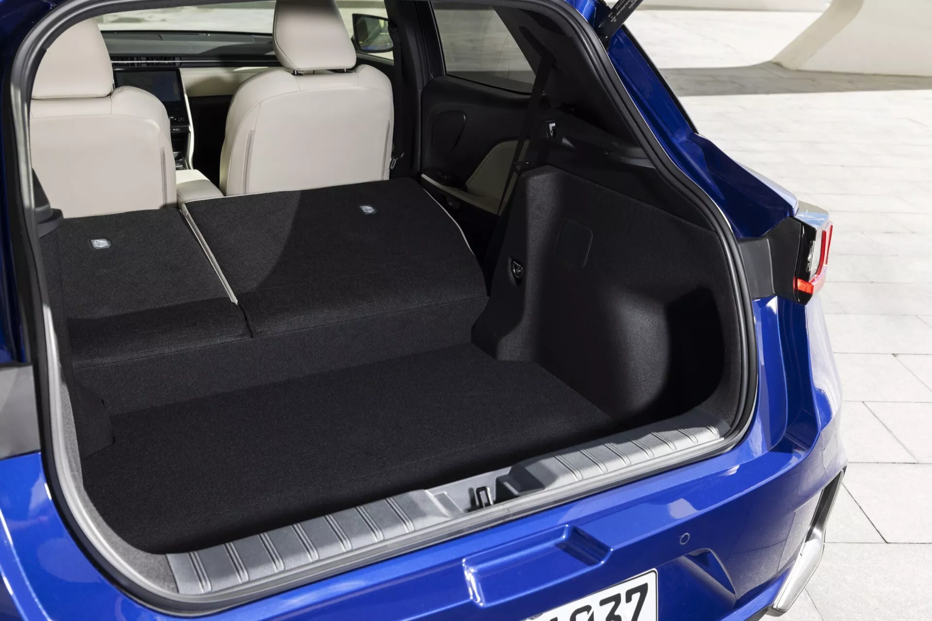 Vue du compartiment arrière du Lexus LBX 1ère génération 2024 avec hayon ouvert, montrant l'espace de chargement spacieux, la protection sur le pare-chocs, conception de siège arrière fractionnable en couleur bleu vif
