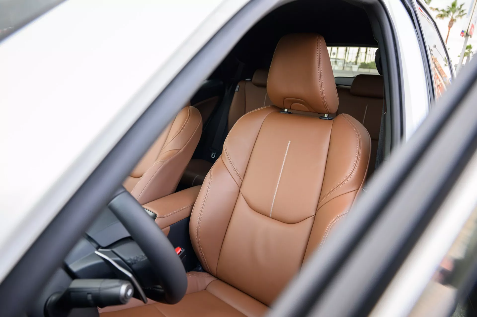 Vue intérieure d'une Lexus LBX 2024 de 1ère génération montrant la zone du conducteur avec des sièges en cuir marron clair de luxe, des commandes de réglage électrique, et des indices de fonctionnalités de haute technologie visibles à travers la porte ouverte du côté conducteur