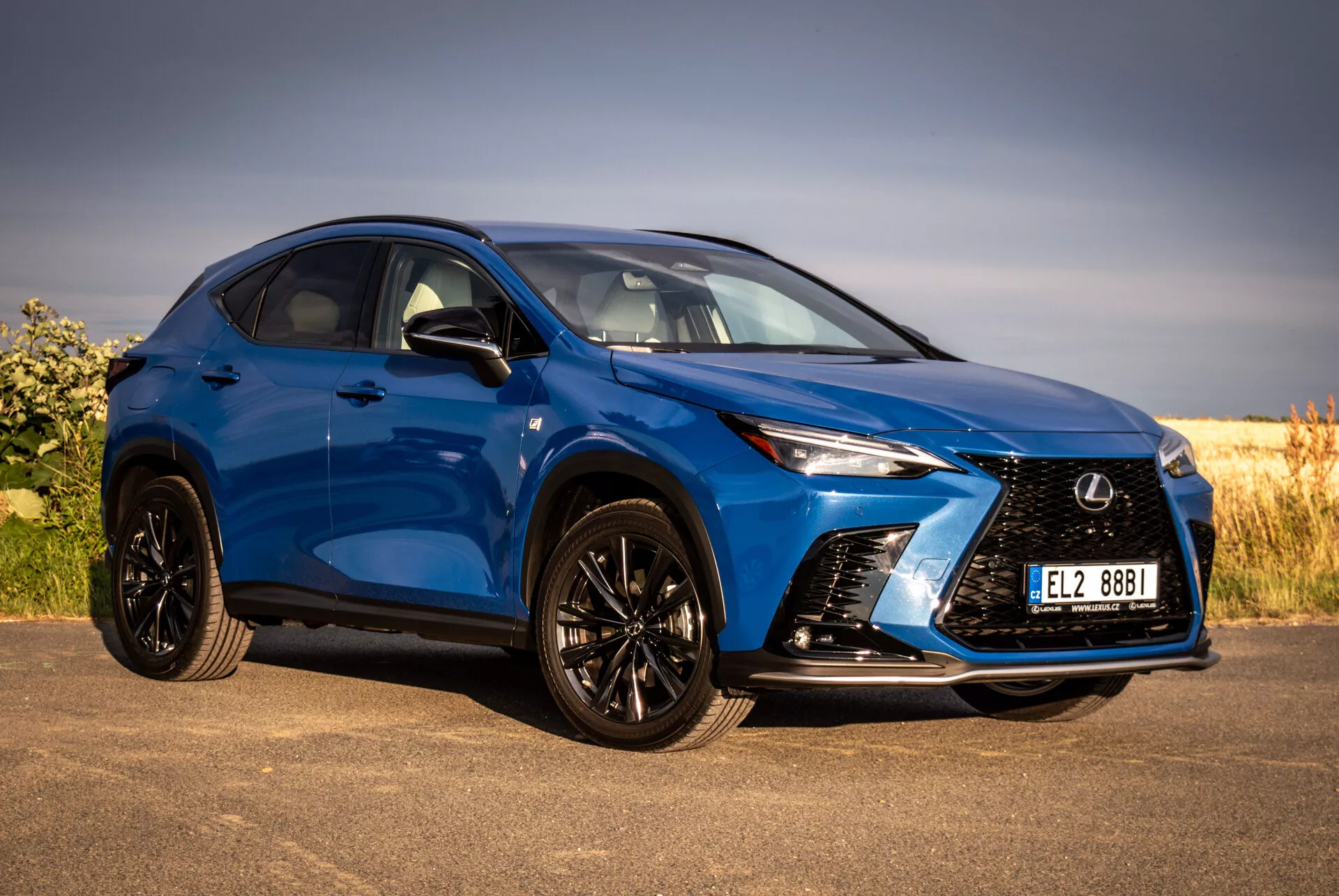 SUV Lexus NX bleu 2021 en vue avant trois quarts soulignant sa grille agressive, ses phares LED aiguisés, ses roues en alliage noir avec pneus à profil bas et ses rétroviseurs latéraux de couleur carrosserie, posé contre un fond naturel