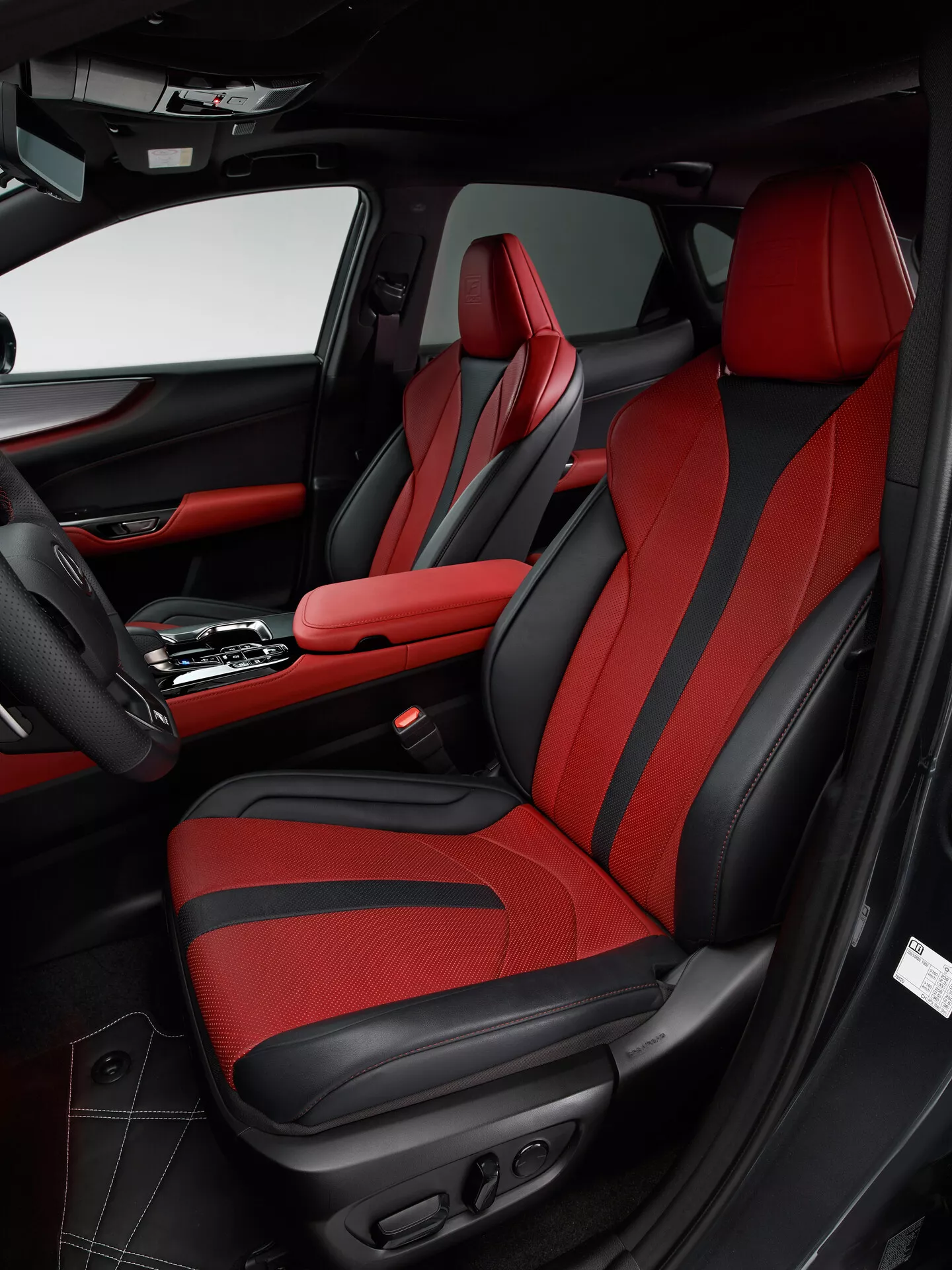 Vue intérieure d'une Lexus NX 2021 montrant la zone passager avant depuis l'angle du côté conducteur. L'image met en valeur le siège passager avec une garniture rouge audacieuse et des accents noirs, avec un design sportif avec des renforts supplémentaires et des commandes de réglage électrique. Le panneau de porte correspond au schéma de couleurs noir et rouge, avec du cuir, du tissu, une poche de rangement, une grille de haut-parleur et divers boutons de commande. La console centrale montre un levier de vitesses automatique et un accoudoir central avec des coutures rouges, reflétant le design luxueux et sportif du véhicule.