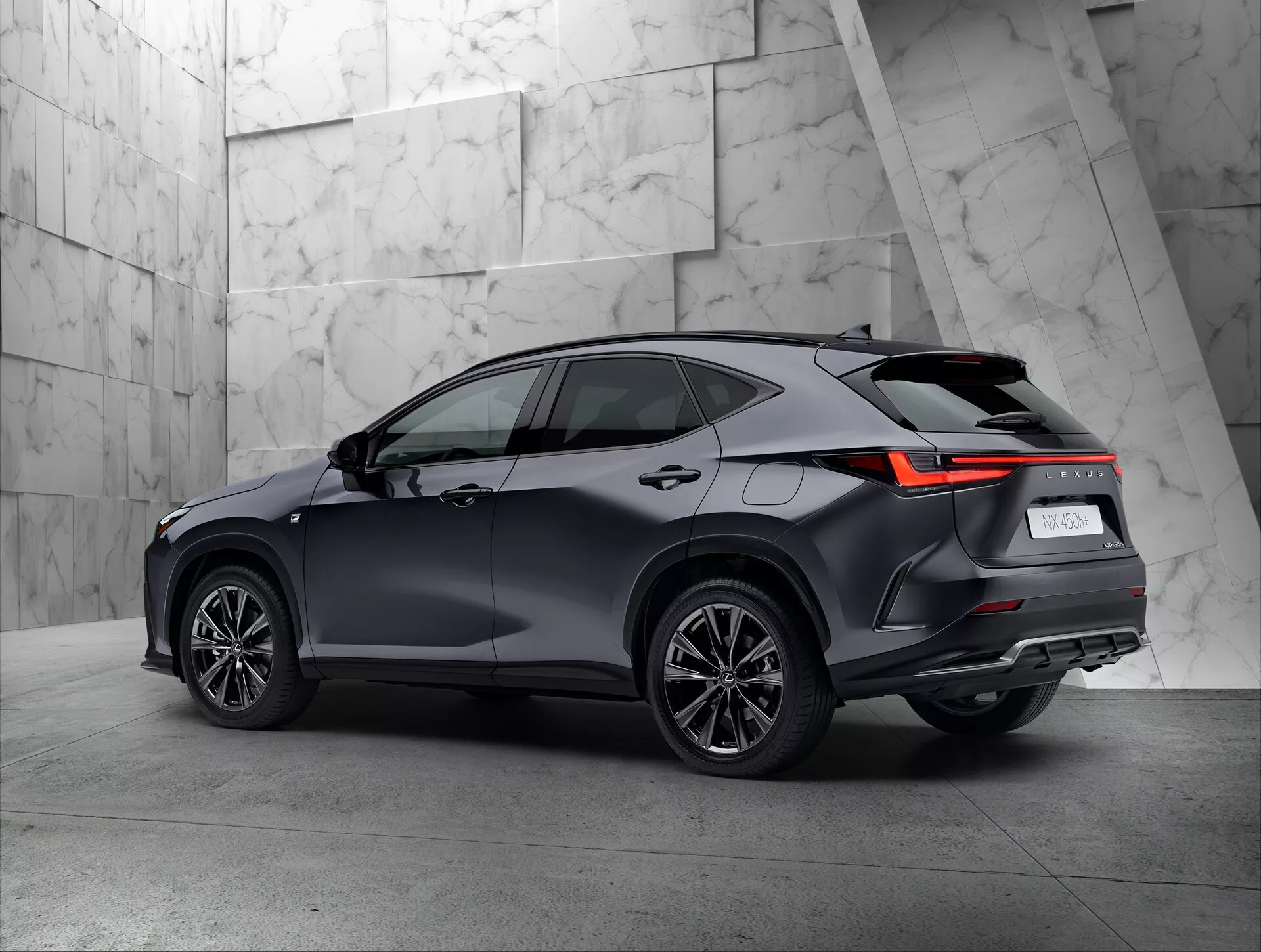 Vue arrière trois quarts d'un SUV moderne Lexus NX 2021 dans un showroom. Le côté droit et l'arrière du véhicule sont bien visibles, mettant en avant les feux arrière avec un design LED angulaire, la peinture sombre et brillante, les roues à rayons multiples et la ligne de toit avec des barres de toit possibles. Le fond neutre et texturé contraste bien avec le design sophistiqué du SUV.