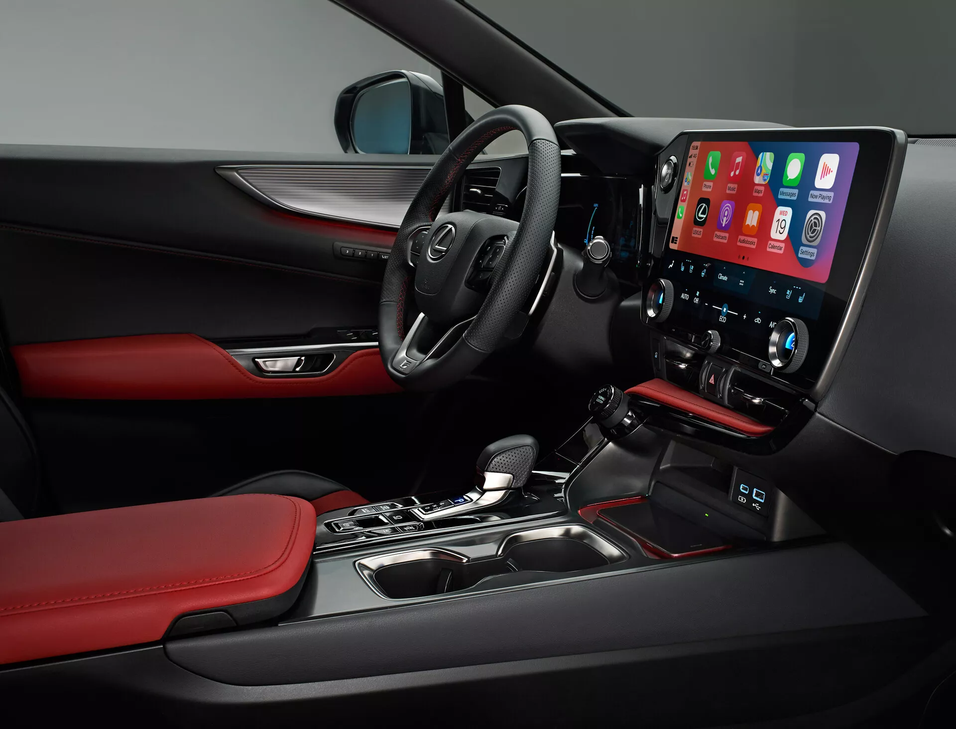 Vue intérieure de la Lexus NX 2021 montrant le côté conducteur. L'image capture le volant multifonction avec commandes intégrées, un tableau de bord partiellement visible et une console centrale proéminente avec un grand écran vertical tactile d'infotainment, probablement affichant Apple CarPlay. Sous l'écran se trouvent les commandes de climat à deux zones. Le levier de vitesse automatique, les matériaux et les détails de conception tels que les surfaces noires avec des accents rouges sur les sièges et les garnitures de portes, et la vue partielle des commandes sur le panneau de porte du conducteur reflètent la nature sportive et premium du véhicule.