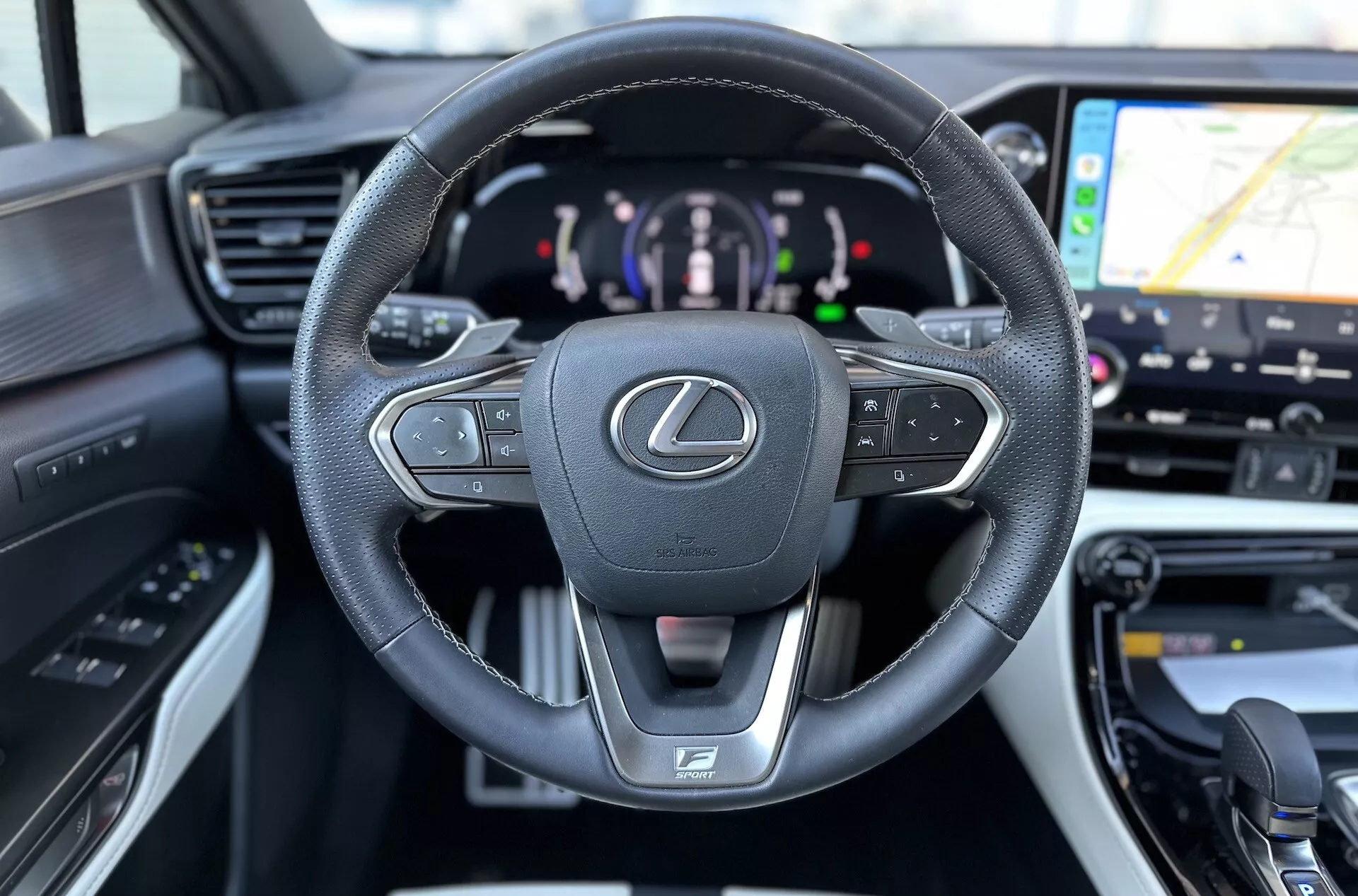 Intérieur du Lexus NX 2021 se concentrant sur le volant multifonction enveloppé de cuir avec emblème Lexus et logo F SPORT, tableau de bord numérique indiquant une motorisation hybride, et aperçu du système de navigation GPS sur le système d'infodivertissement