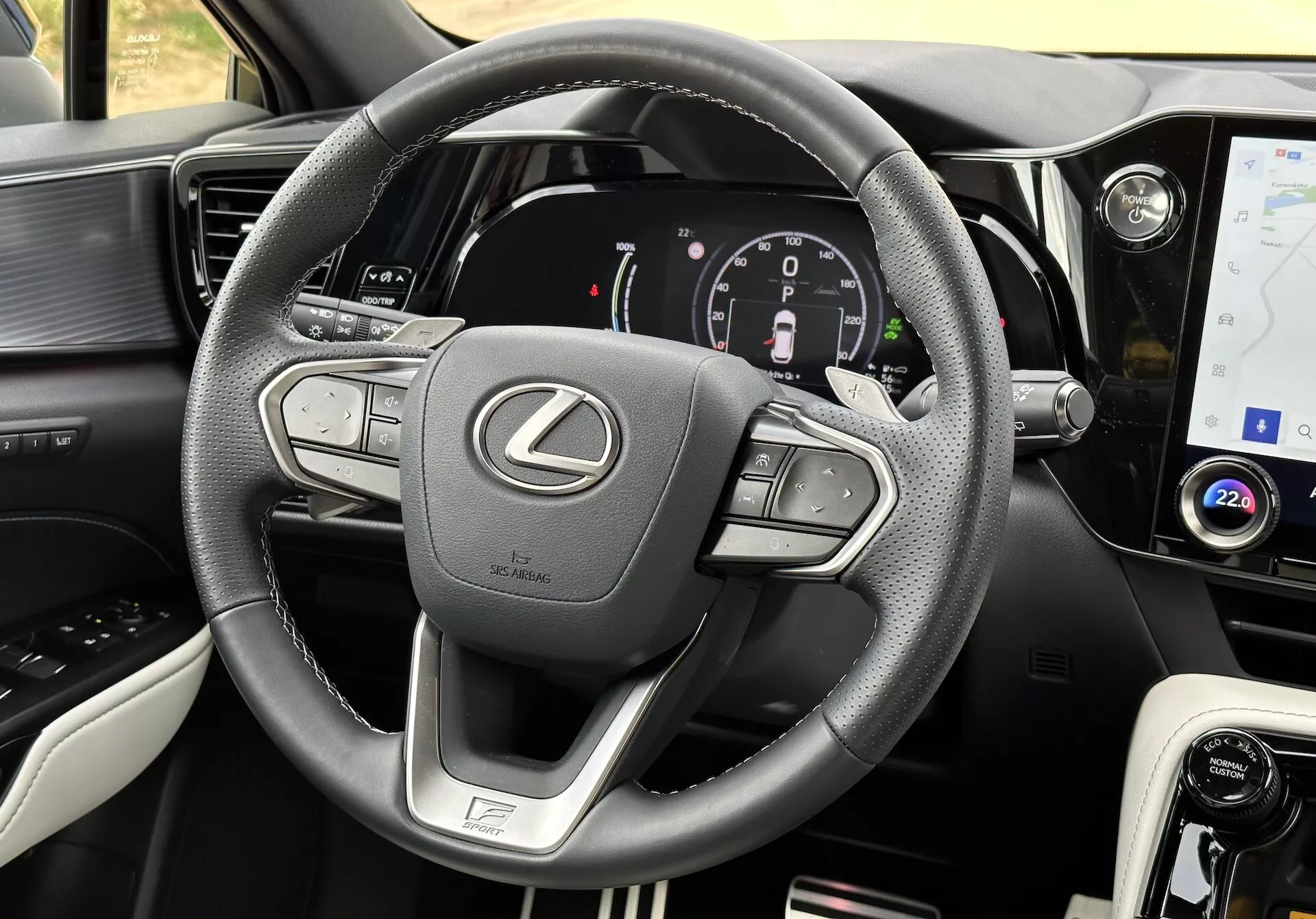 Vue intérieure d'une Lexus NX 2021 axée sur le volant et le tableau de bord, présentant des boutons multifonctions, un tableau de bord numérique, un écran tactile infotainment, des accents en cuir, un sélecteur de mode de conduite, des aérations d'air et des coutures détaillées.