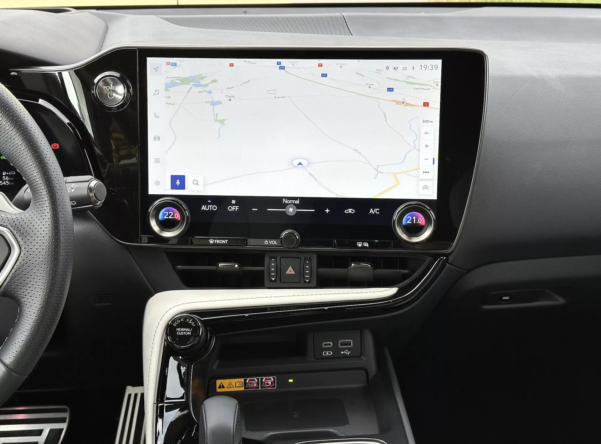 Console centrale du Lexus NX 2021 avec écran tactile affichant la navigation GPS, les boutons et les cadrans de commande climatique, et le compartiment de chargement pour smartphone