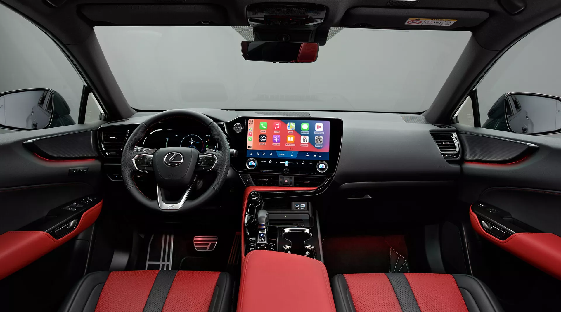 Intérieur du Lexus NX 2021, centré sur l'habitacle avant, pris depuis une position centrale. La perspective grand-angle montre le tableau de bord avec un grand écran tactile central d'infodivertissement affichant une interface mobile, des commandes physiques pour le climatiseur et un levier de vitesses pour la transmission automatique. Le volant multifonctions avec des boutons de commande suggère des fonctionnalités avancées. Les sièges sont habillés de cuir bicolore rouge et noir, offrant un aspect sportif. Les panneaux de porte correspondent au thème rouge et noir avec des commandes pour les vitres électriques et une grille de haut-parleur visible, soulignant la modernité et le luxe.