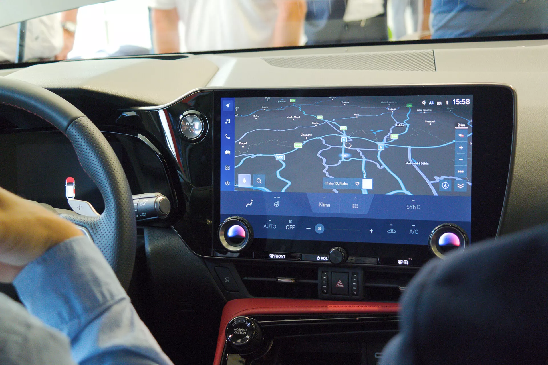 Vue intérieure d'une voiture moderne se concentrant sur la console centrale et le système d'infodivertissement depuis la perspective du passager, montrant un grand écran tactile avec une carte de navigation, des commandes physiques pour les fonctions de climatisation, un panneau noir brillant avec un accent rouge, et suggérant un design convivial pour le conducteur dans un environnement animé.