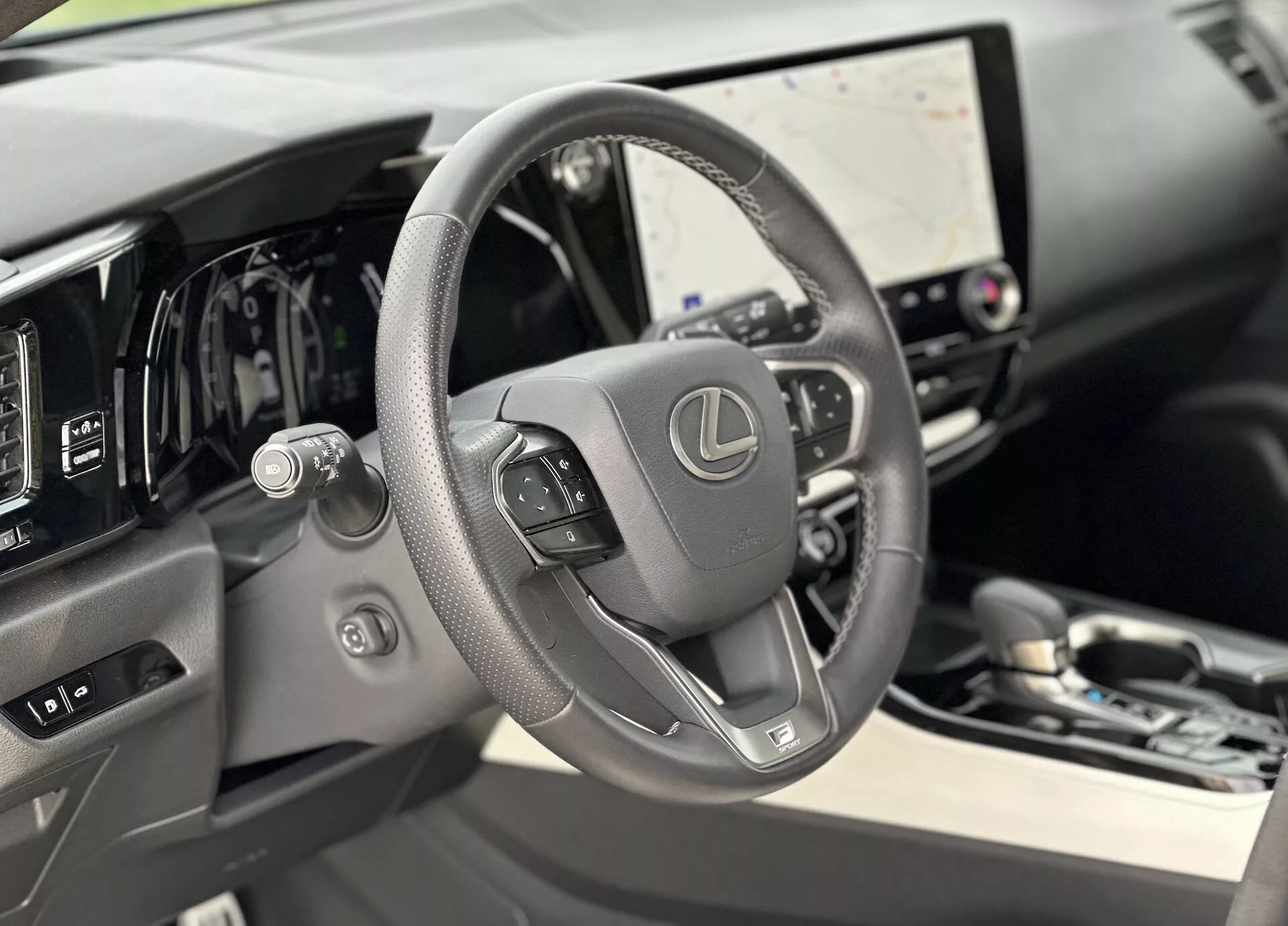 Vue intérieure du Lexus NX 2021 se concentrant sur le volant en cuir avec commandes intégrées et tableau de bord numérique derrière, présentant un grand écran tactile d'infodivertissement et des indices subtils de luxe dans les matériaux de haute qualité