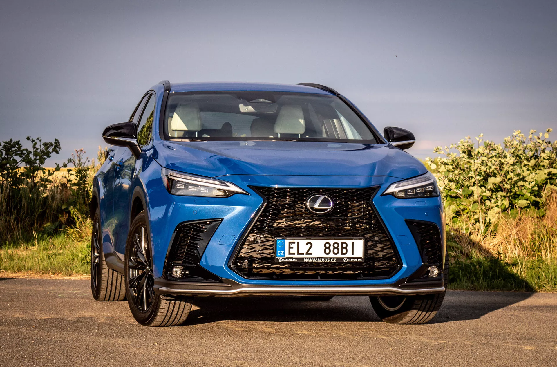 Vue de face d'un SUV Lexus NX 2021 bleu soulignant sa grille à fuseau complexe, phares LED angulaires, finition brillante et conception aérodynamique, stationné en extérieur sous un ciel dégagé