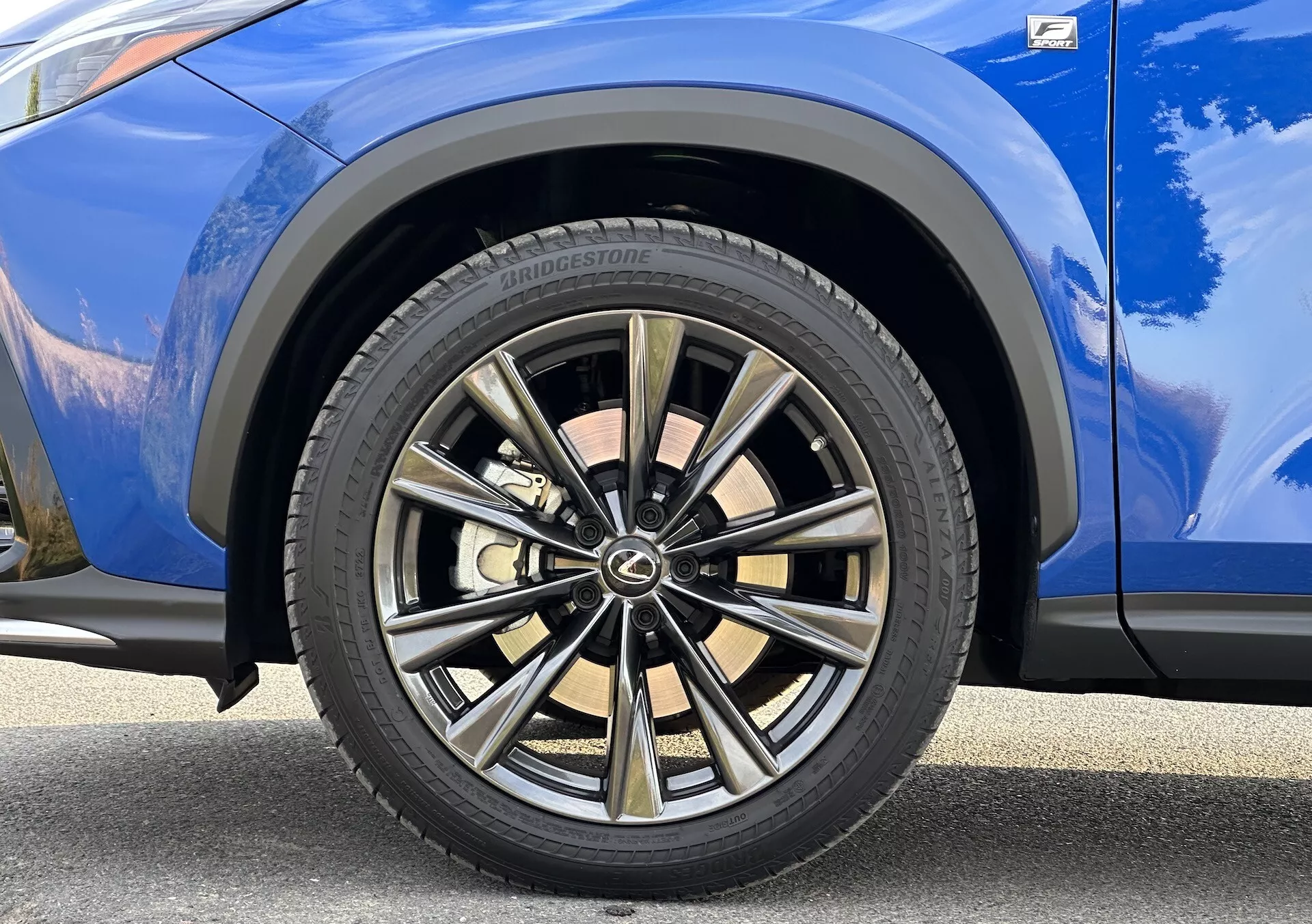 Vue détaillée de la roue avant côté passager de la Lexus NX 2021 avec design à plusieurs branches en finition bicolore et pneu Bridgestone, sur une carrosserie bleue vibrante