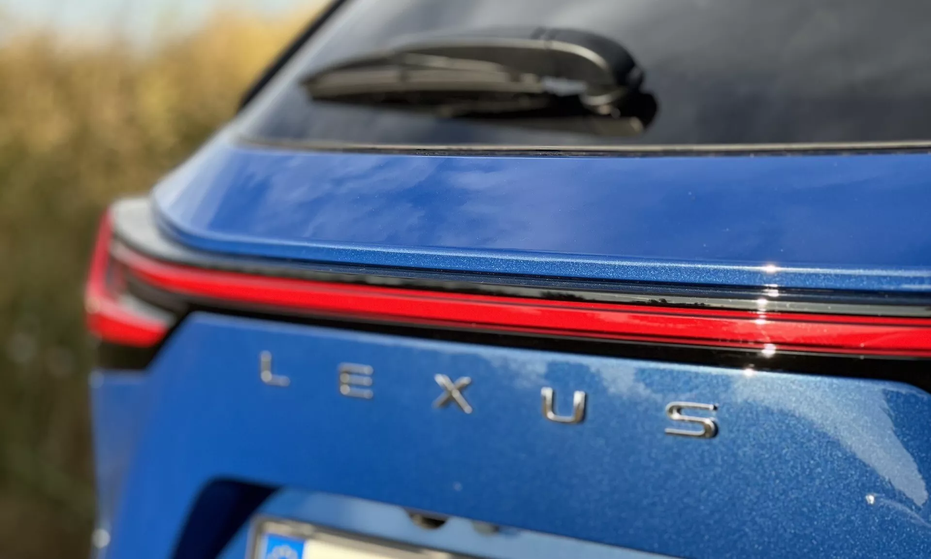 Vue rapprochée de la zone de marquage arrière du Lexus NX 2021 avec un badge Lexus argenté, une bande lumineuse rouge au-dessus du nom, sur une carrosserie bleu métallique sous conditions de lumière du jour