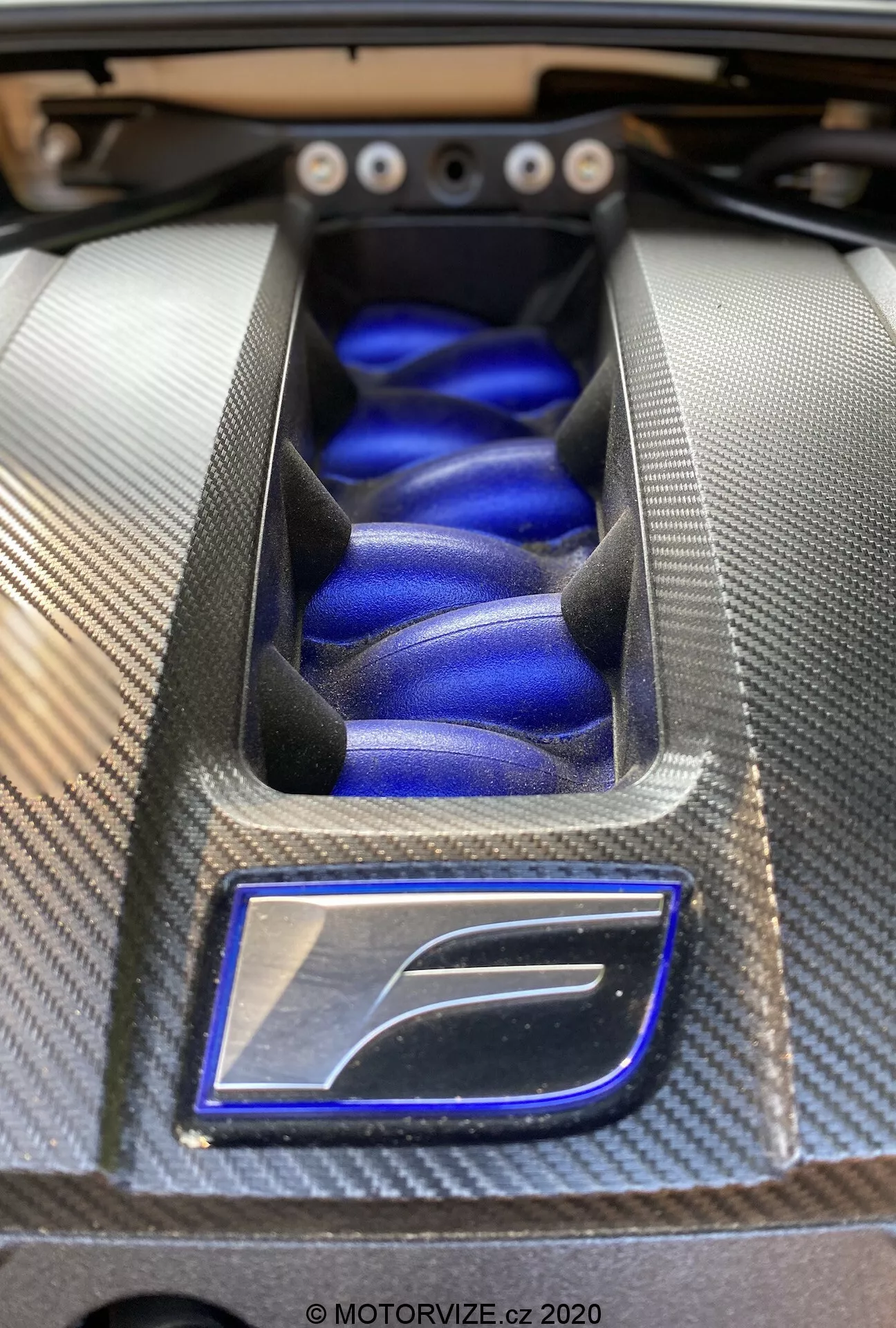 Vue rapprochée du compartiment moteur haute performance de la Lexus RC 2016, mettant en valeur un cache moteur stylisé avec un entourage en fibre de carbone texturé et une finition bleue vibrante, illustrant l'ingénierie et le design automobile haut de gamme.