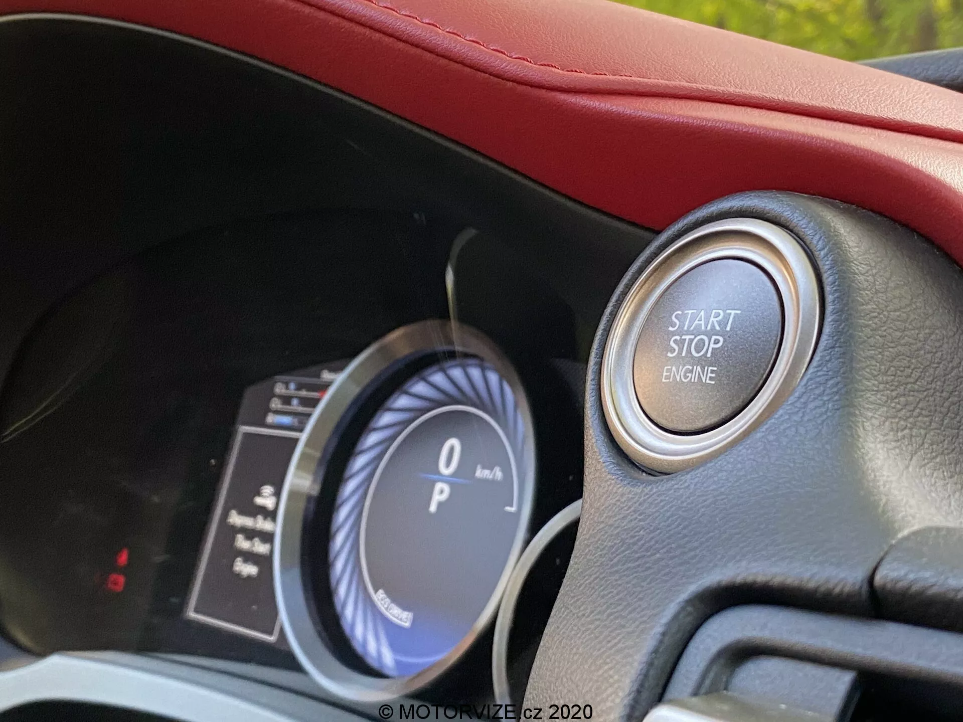 Vue rapprochée de l'intérieur du Lexus RC 2016 de la perspective du conducteur, présentant un tableau de bord analogique numérique avec un compteur de vitesse affichant '0 km/h' et une jauge de carburant. L'accent est mis sur le système d'allumage moderne par bouton-poussoir marqué 'START STOP ENGINE' entouré d'un anneau métallique, indicatif d'un véhicule haut de gamme avec démarrage sans clé. L'habitacle bien éclairé présente des indices de rembourrage rouge et des technologies avancées pour l'intérieur du véhicule.