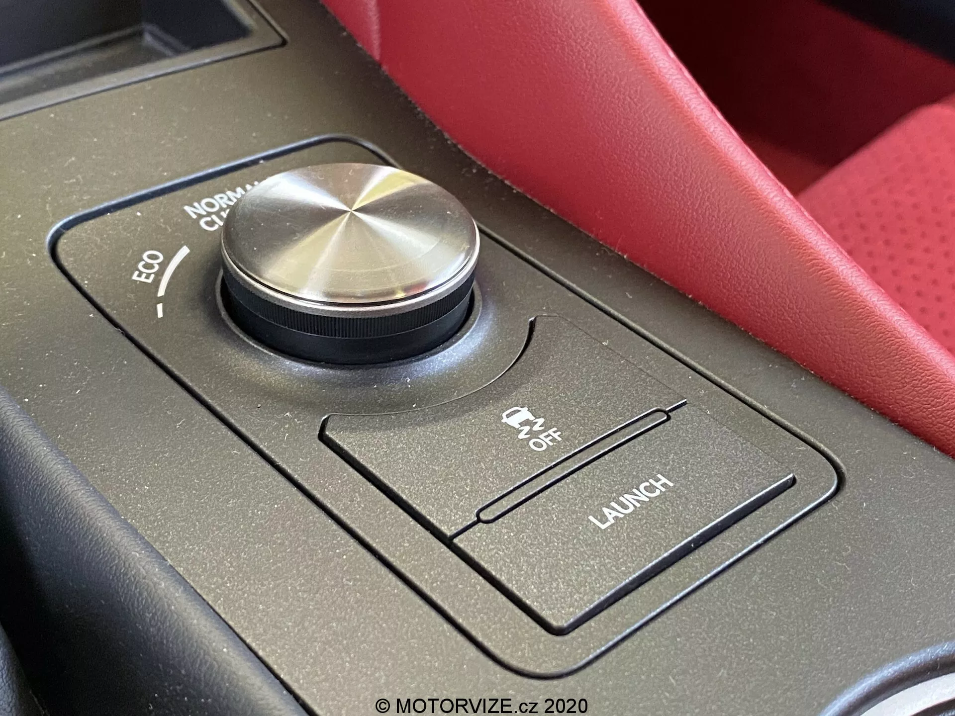 Gros plan de la zone du sélecteur de mode de conduite à l'intérieur d'une Lexus RC 2016, montrant un grand sélecteur de mode de conduite avec finition métallique usinée et bords moletés. Le sélecteur affiche les modes 'ECO,' 'NORMAL,' 'COMFORT' et un mode sportif partiellement masqué. Autour du sélecteur se trouvent des commandes supplémentaires sur une surface noire mate, y compris un interrupteur 'CTX OFF' pour le contrôle de traction et un bouton 'LAUNCH' pour le contrôle de lancement. L'image capture la console centrale de la perspective du siège du conducteur, mettant en valeur les caractéristiques intérieures haut de gamme et orientées performance.