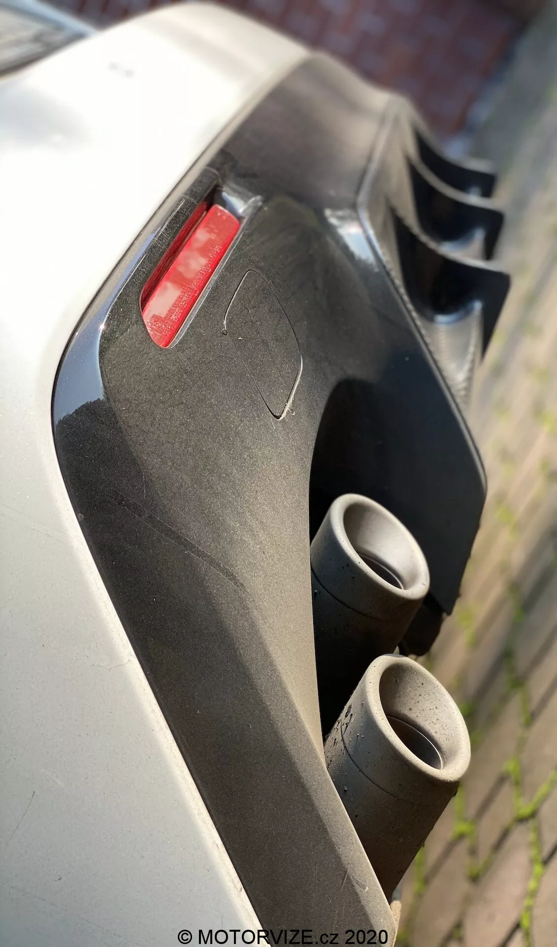 Vue arrière en gros plan et en angle d'une Lexus RC 2016 se concentrant sur les doubles tuyaux d'échappement métalliques et le diffuseur aérodynamique arrière, avec un panneau de carrosserie blanc et un feu arrière rouge visibles. Le système d'échappement et le diffuseur mettent en évidence les caractéristiques de performance et aérodynamiques, capturées d'une perspective basse avec une faible profondeur de champ.
