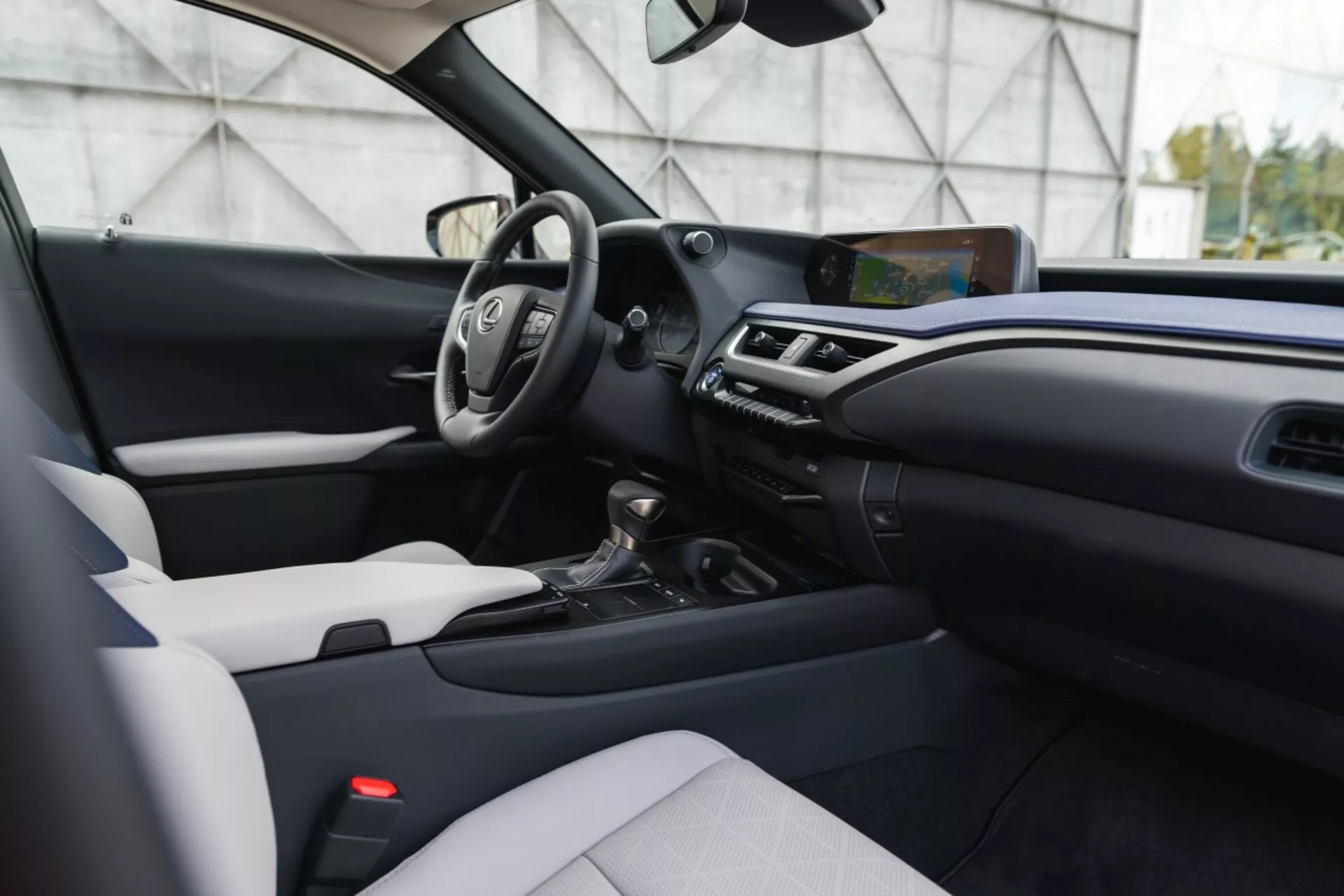 Vue intérieure du Lexus UX 2019 depuis la perspective du passager avant montrant le tableau de bord, la console centrale, le siège du conducteur avec volant et affichages numériques, système d'infodivertissement tactile, commande de climatisation, sélecteur de vitesse, siège passager avec garniture bicolore, et accents de finition modernes.