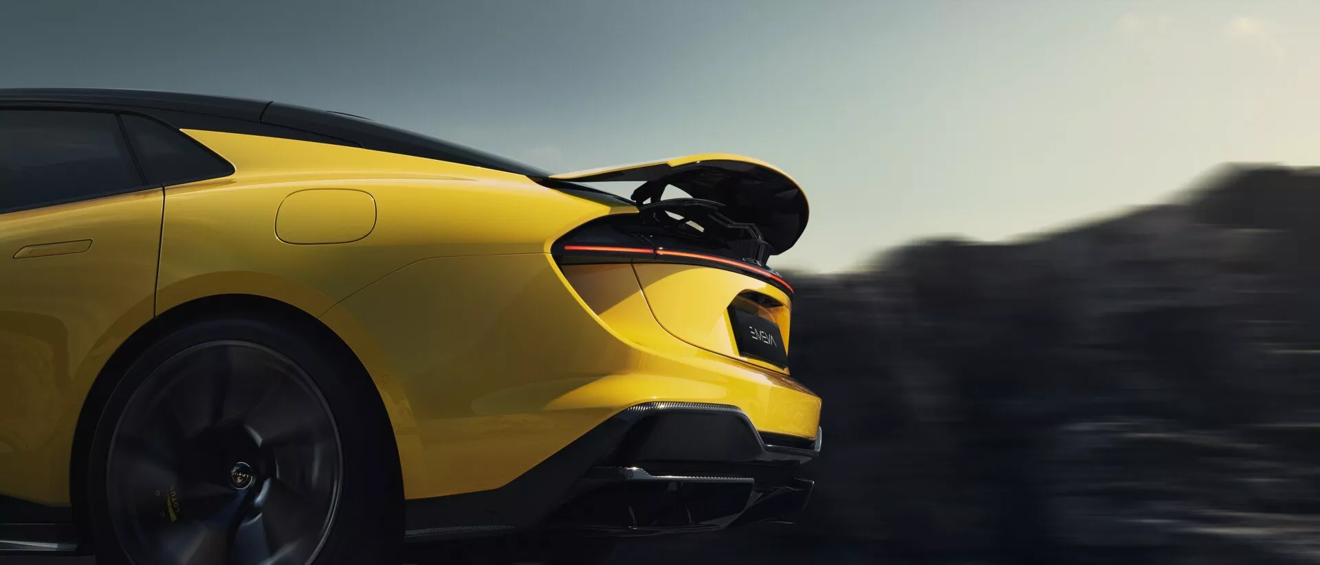 Lotus Emeya 2024 démontrant son design aérodynamique et sa stature sportive, avec un focus sur le côté droit, grand aileron arrière et feux arrière LED, sur un fond flou de mouvement
