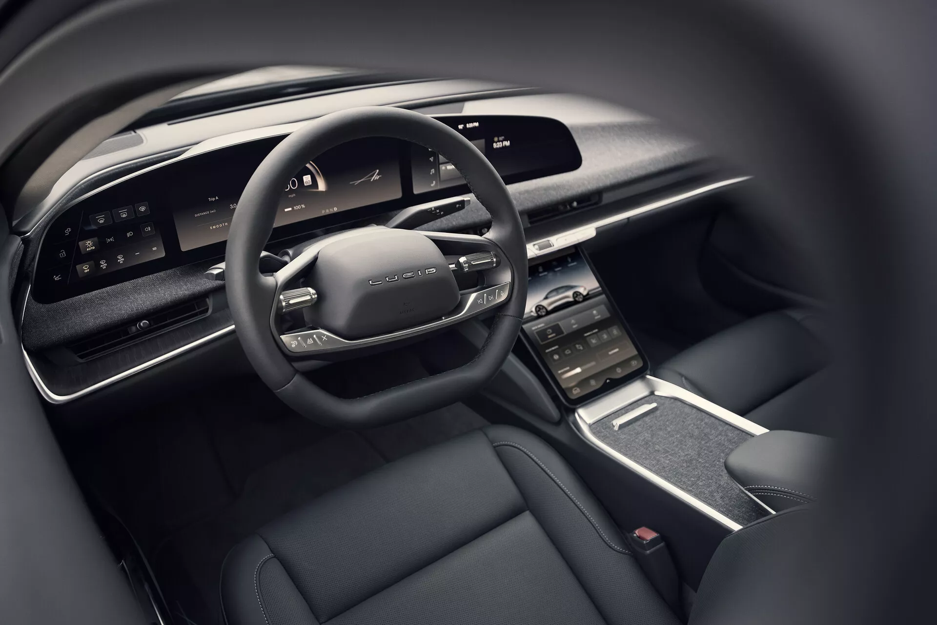 Vue rapprochée de l'habitacle du conducteur de la Lucid Air 2022 depuis la perspective du siège arrière, montrant le volant multifonction moderne avec commandes, le large tableau de bord numérique, l'écran tactile central vertical entouré de bouches d'air, la console centrale élégante avec un minimum de boutons physiques et un intérieur luxueux avec un schéma de couleurs sombres comprenant des matériaux de haute qualité.