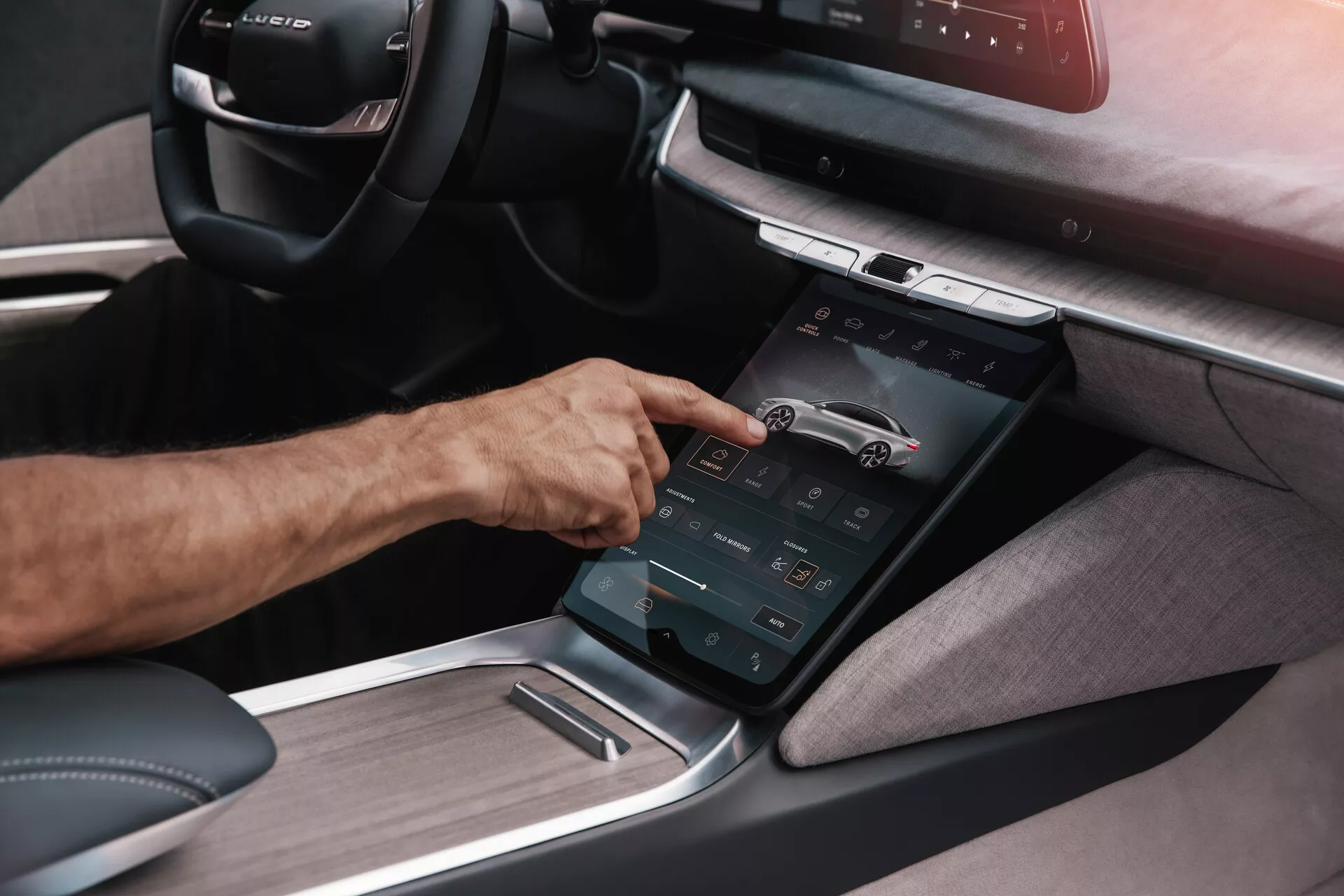 Vue détaillée de la console centrale de la première génération de Lucid Air 2022 sous un angle oblique, mettant en évidence un écran tactile vertical avec lequel une main droite interagit, illustrant le système d'infodivertissement avancé avec divers contrôles fonctionnels et un habillage combiné de textile et de métal, suggérant un design intérieur moderne, luxueux et axé sur une technologie de pointe.