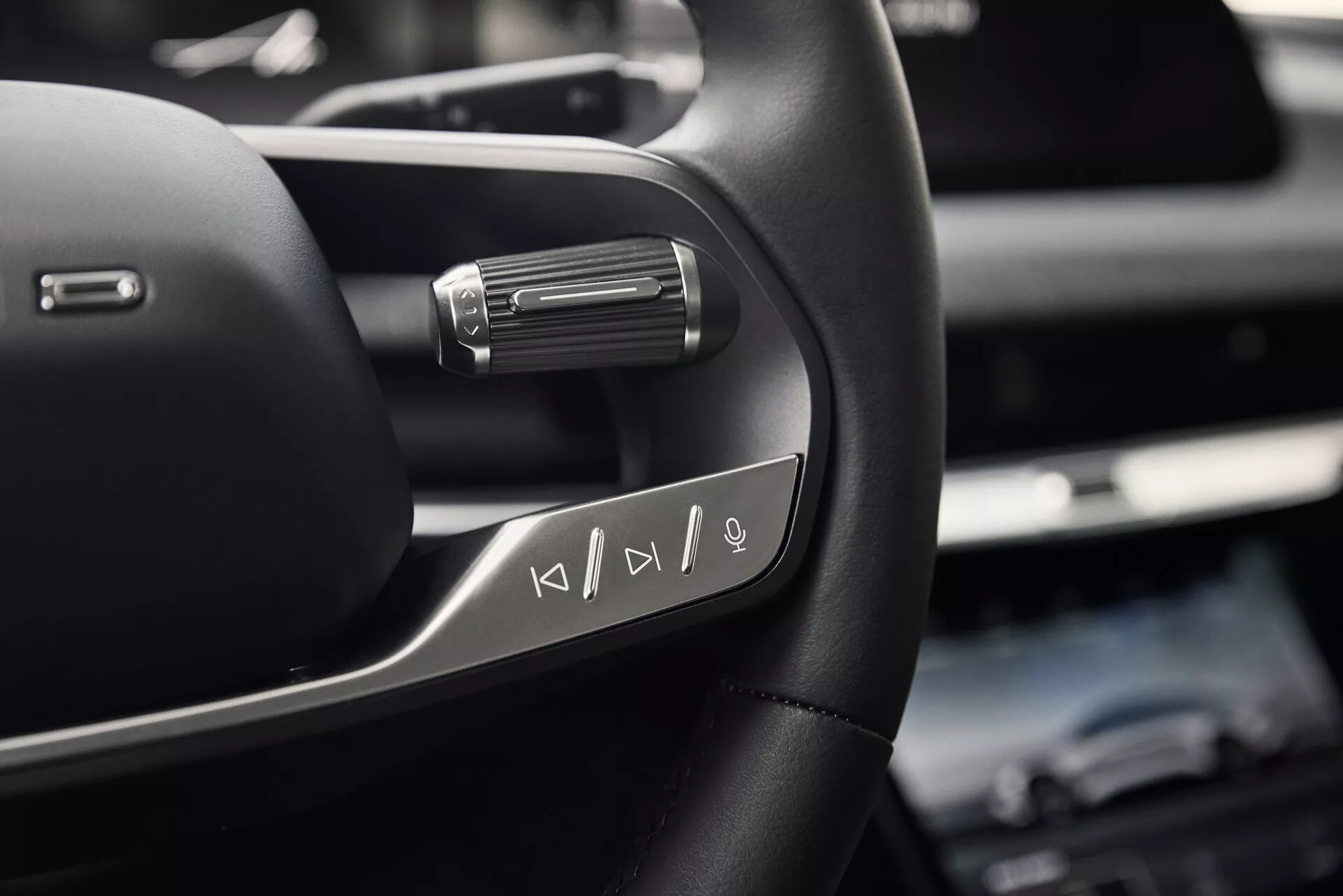 Vue rapprochée du côté gauche du volant du Lucid Air 2022, montrant des boutons de commande multimédia multifonctions. La photo, prise en dessous du volant au niveau de la poitrine d'un conducteur assis, met en avant le matériau en cuir de haute qualité avec des accents métalliques et une palette derrière le volant, indiquant des fonctionnalités de conduite avancées.