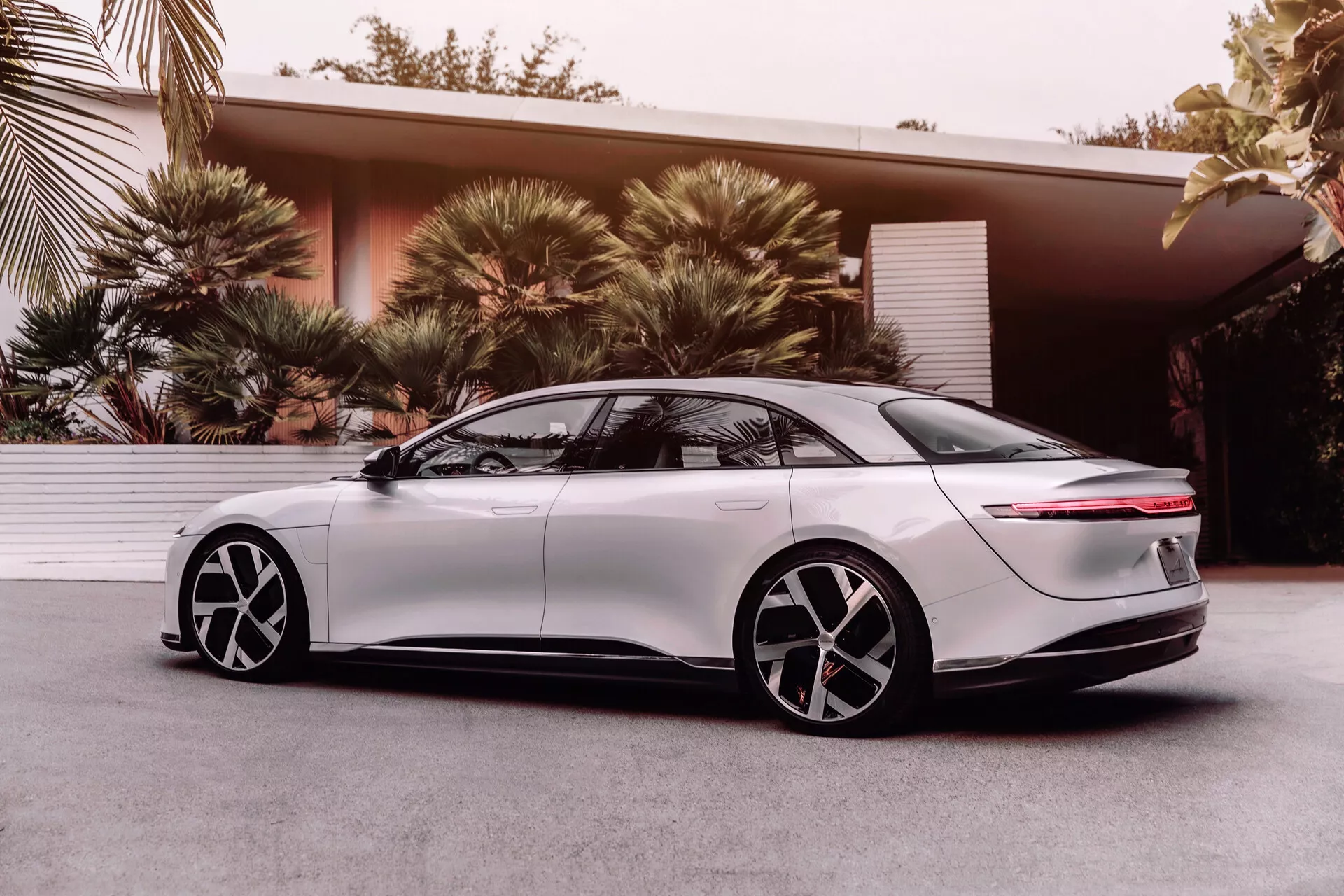 Berline électrique Lucid Air 2022, 1ère génération, vue de profil latéral sous un angle bas mettant en avant le design aérodynamique, phares à LED élégants, aile avant lisse, poignées de porte encastrées rétractables, jantes alliage bicolores à cinq branches, vitres teintées, arrière fastback avec bande lumineuse horizontale et spoiler intégré, illustrant la technologie et le design moderne des véhicules électriques.
