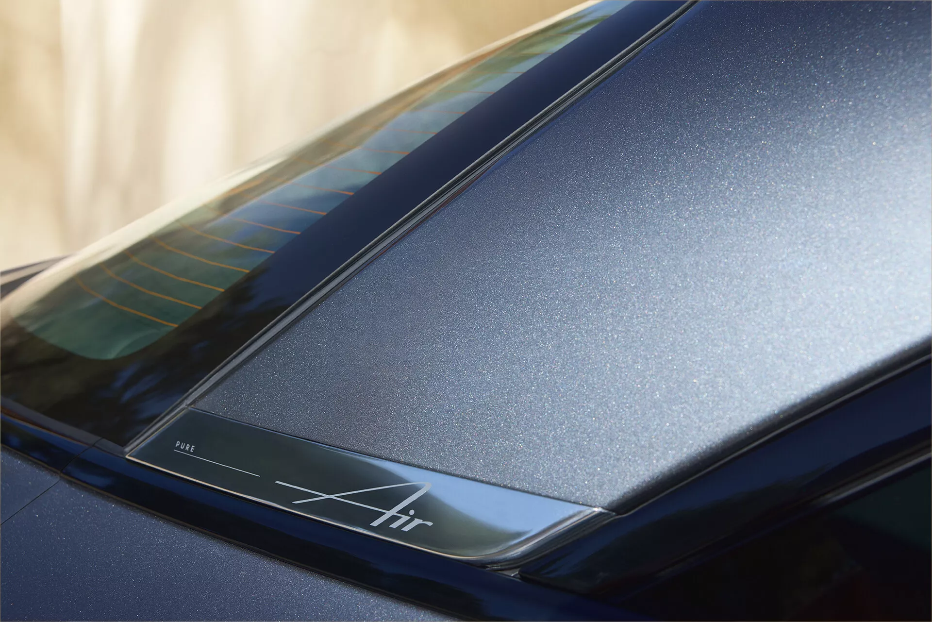 Gros plan sur la section arrière près du toit d'une Lucid Air 2022 (1ère génération), mettant en avant la finition bleu foncé brillante et les lignes aérodynamiques élégantes. Met en évidence une bande rétroéclairée avec l'inscription 'Air', soulignant le design luxueux et la technologie avancée potentielle.