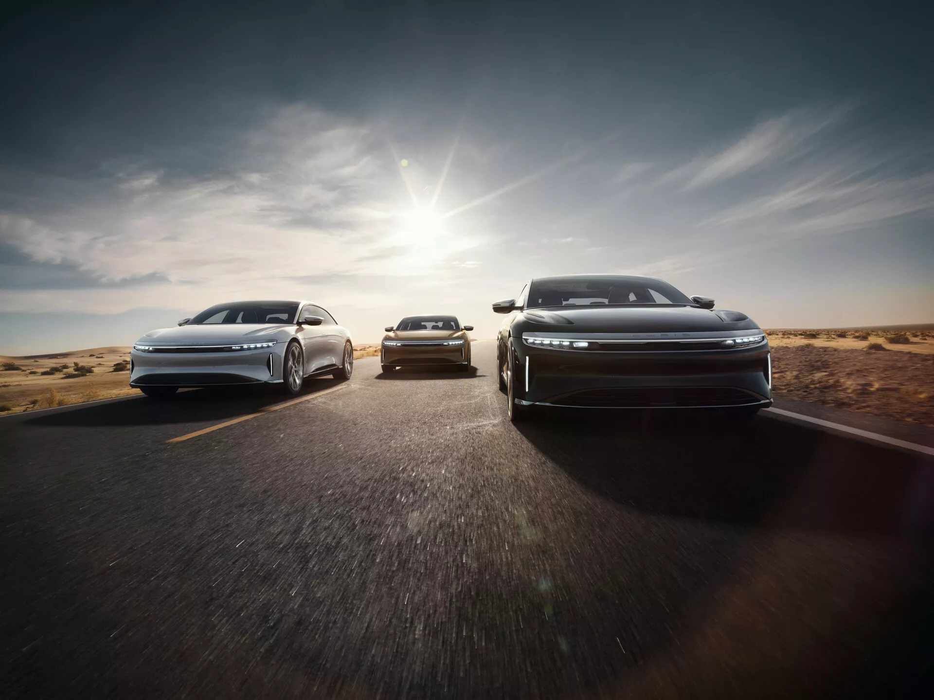 Vue avant de la Lucid Air 2022 avec design aérodynamique et phares LED en formation échelonnée sur route asphaltée avec arrière-plan désertique, la lumière du soleil projetant une lueur chaude