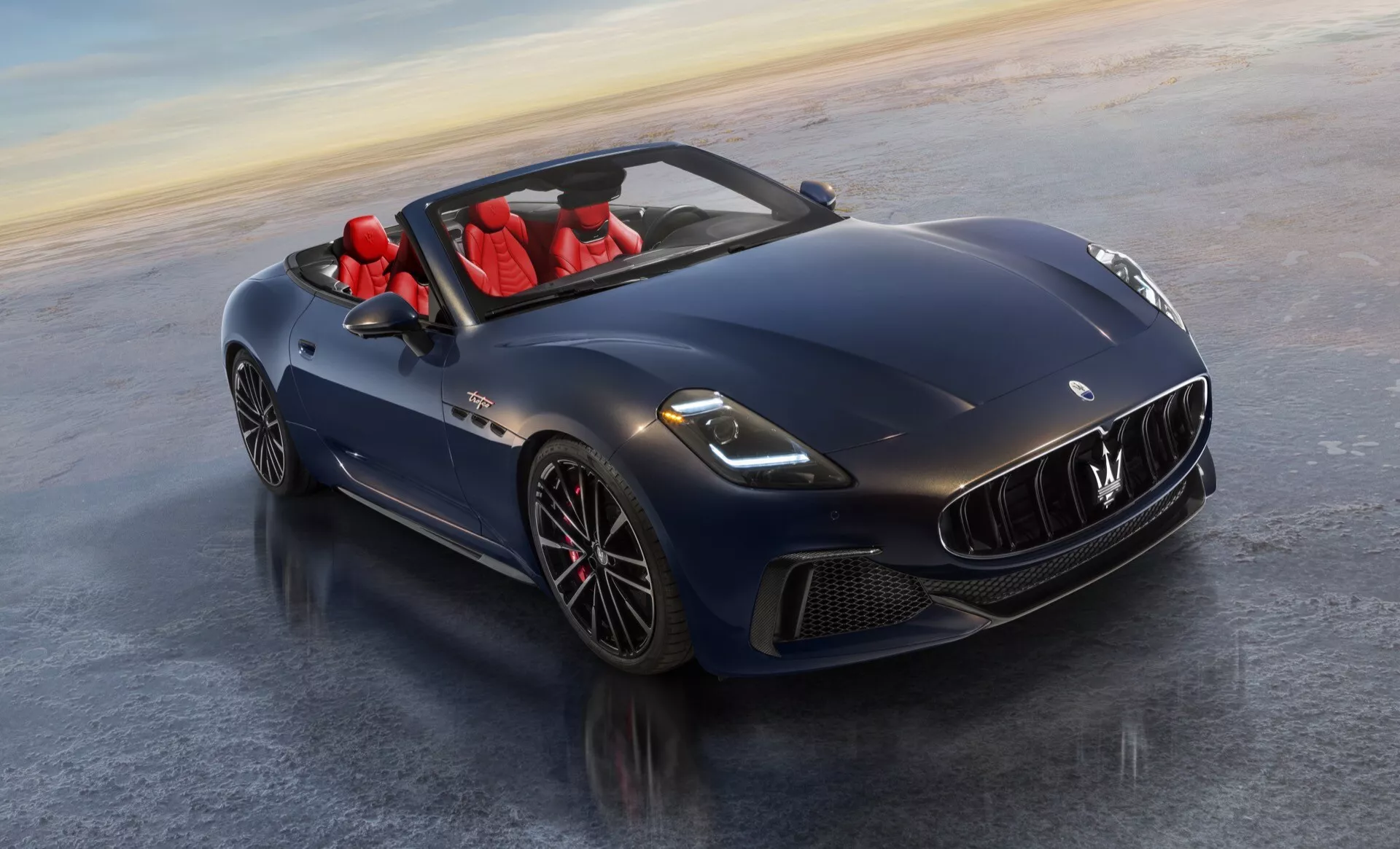 Maserati GranCabrio 2ème génération 2024 en bleu profond avec intérieur rouge, présentant des phares LED, design aérodynamique, toit convertible, grille avant et jantes en alliage depuis un angle avant trois quarts élevé.