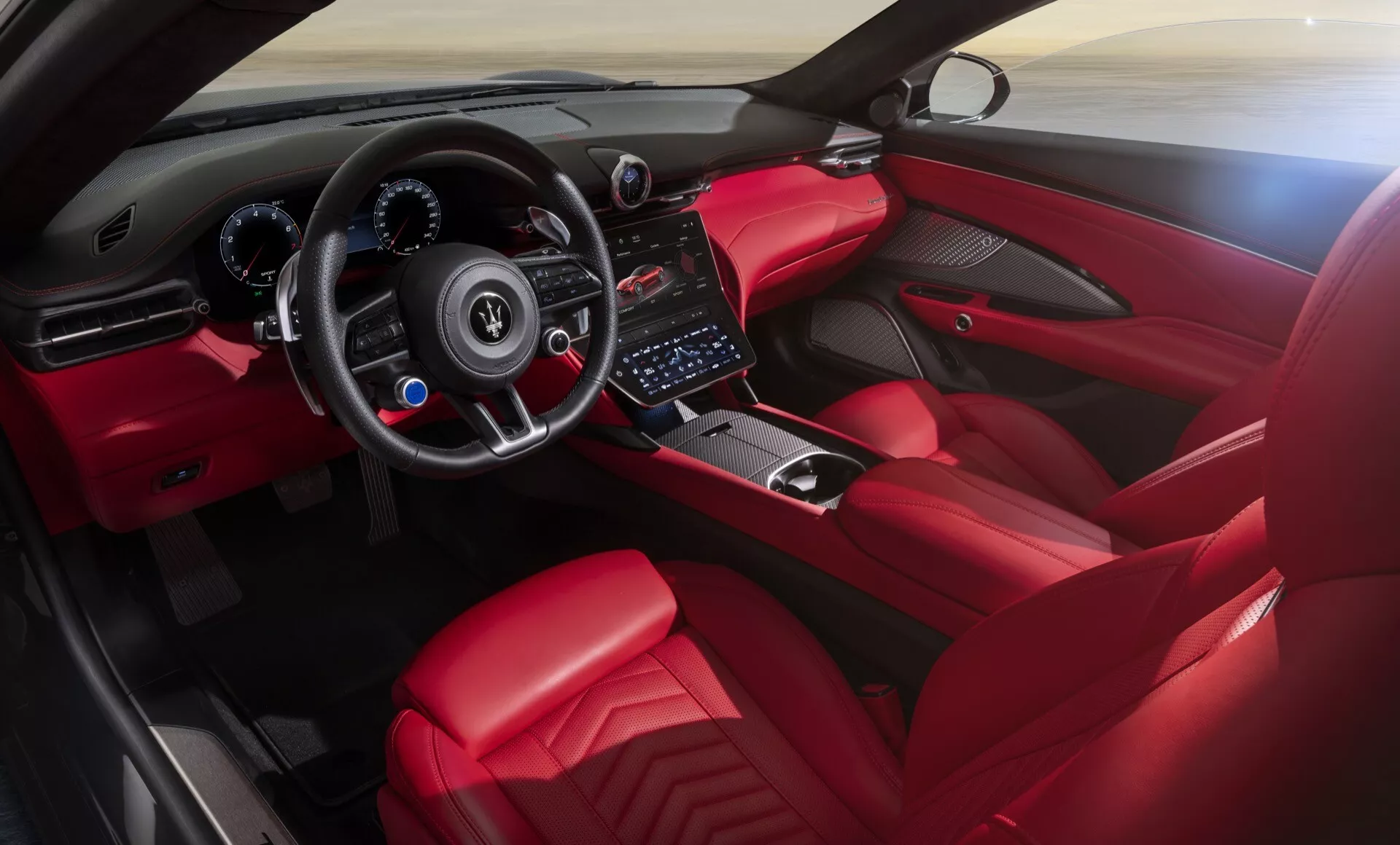 Vue intérieure de la Maserati GranCabrio 2ème génération 2024 axée sur le cockpit et le tableau de bord, présentant un volant sportif à fond plat avec boutons de contrôle, des clusters d'instruments digitaux derrière le volant, un écran tactile d'infodivertissement au centre, des boutons minimalistes pour le contrôle du climat, un sélecteur de vitesse indiquant une transmission automatique ou manuelle séquentielle entouré de boutons de contrôle pour les modes de conduite, et un rembourrage rouge premium avec des accents en fibre de carbone et des finitions en métal brossé.
