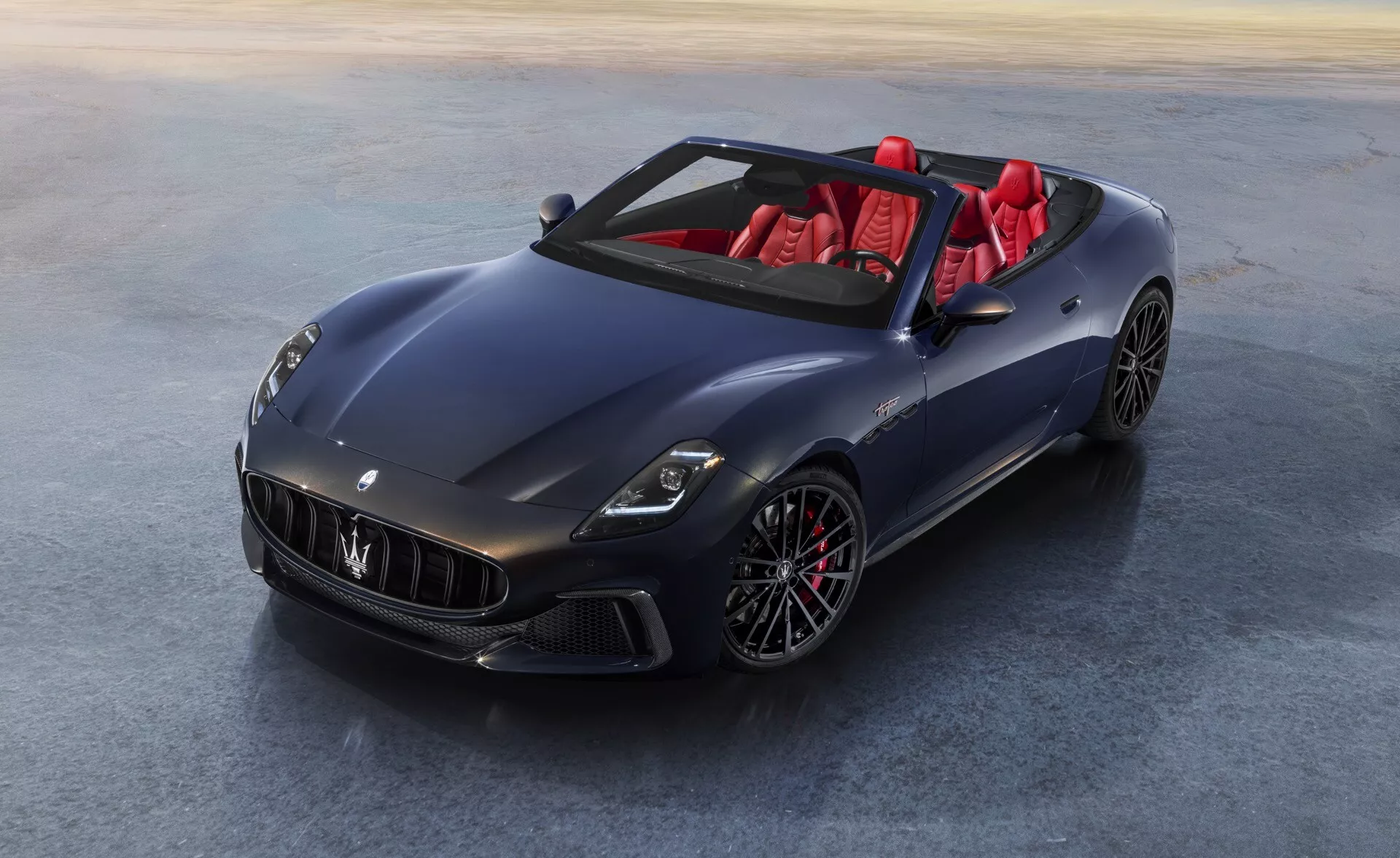 Maserati GranCabrio 2ème génération 2024 en bleu foncé métallisé ou gris avec phares LED, jantes alliage multi-branches, intérieur rouge et finition haut brillant, capturée depuis une vue aérienne frontale mettant en lumière les caractéristiques de luxe et de performance de la voiture.