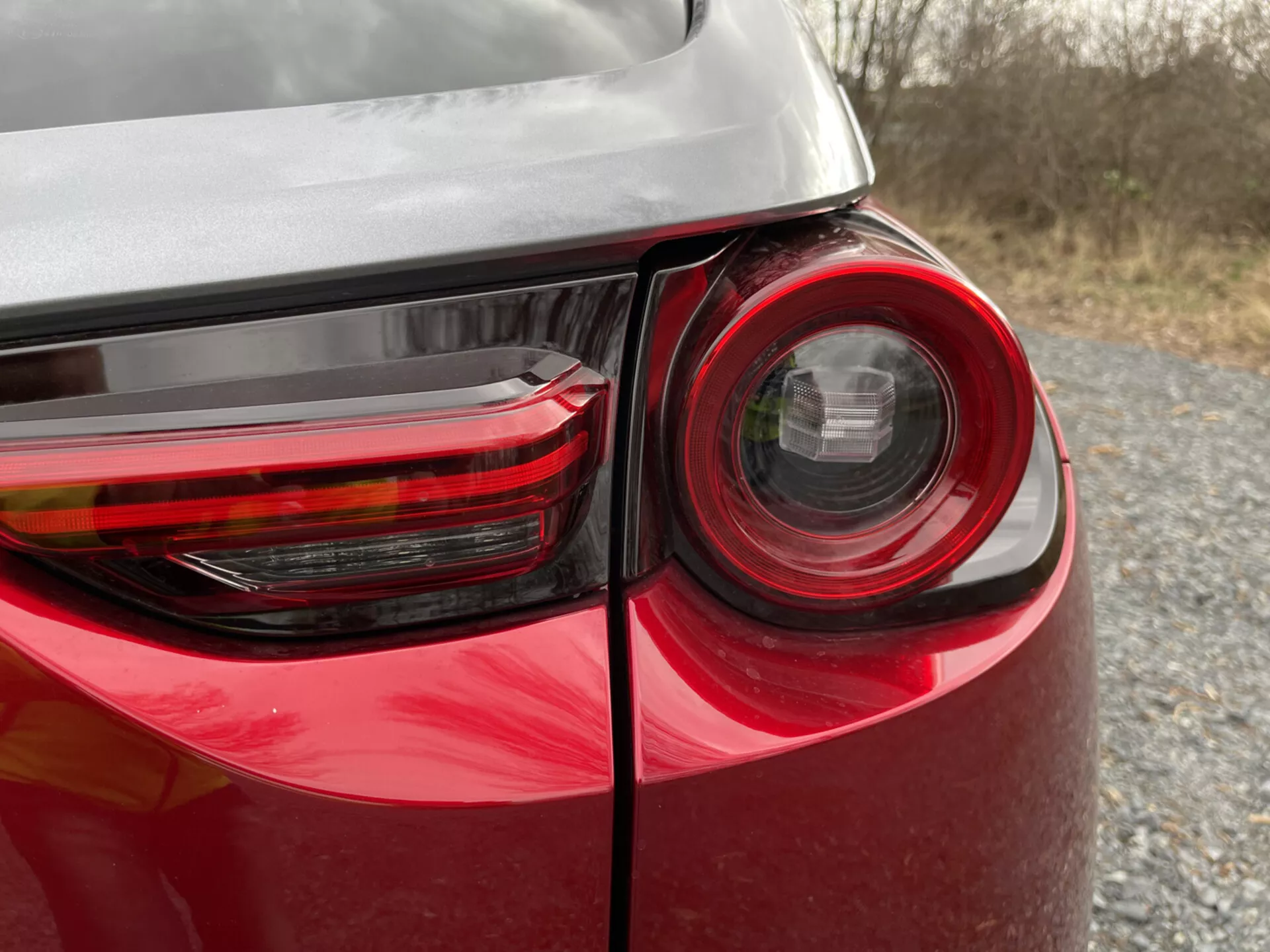 Vue rapprochée du coin arrière d'une Mazda MX-30 2020 montrant le design détaillé du feu arrière, la peinture rouge brillante et le reflet sur sa carrosserie, mettant en évidence la technologie d'éclairage et le design des véhicules modernes.