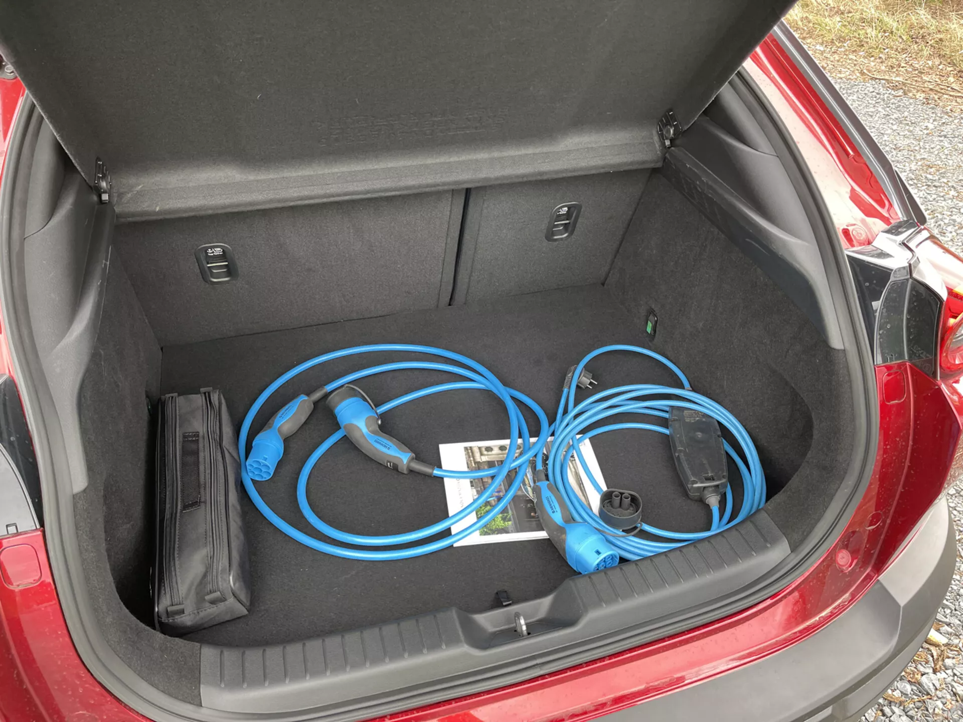 Coffre ouvert de la Mazda MX-30 2020 affichant un câble de charge pour véhicule électrique portable avec une vue rapprochée de haut en bas depuis la gauche, mettant en avant l'espace de rangement propre et plat ainsi que des compartiments intérieurs.