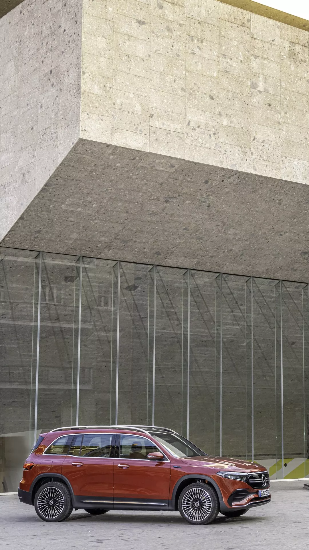 SUV Mercedes EQB 2021 garé sur le trottoir avec un bâtiment architectural en arrière-plan, montrant le côté avant gauche avec une calandre chromée proéminente, des phares LED élégants, un capot sculpté, des roues en alliage, des vitres teintées et des rails de toit.