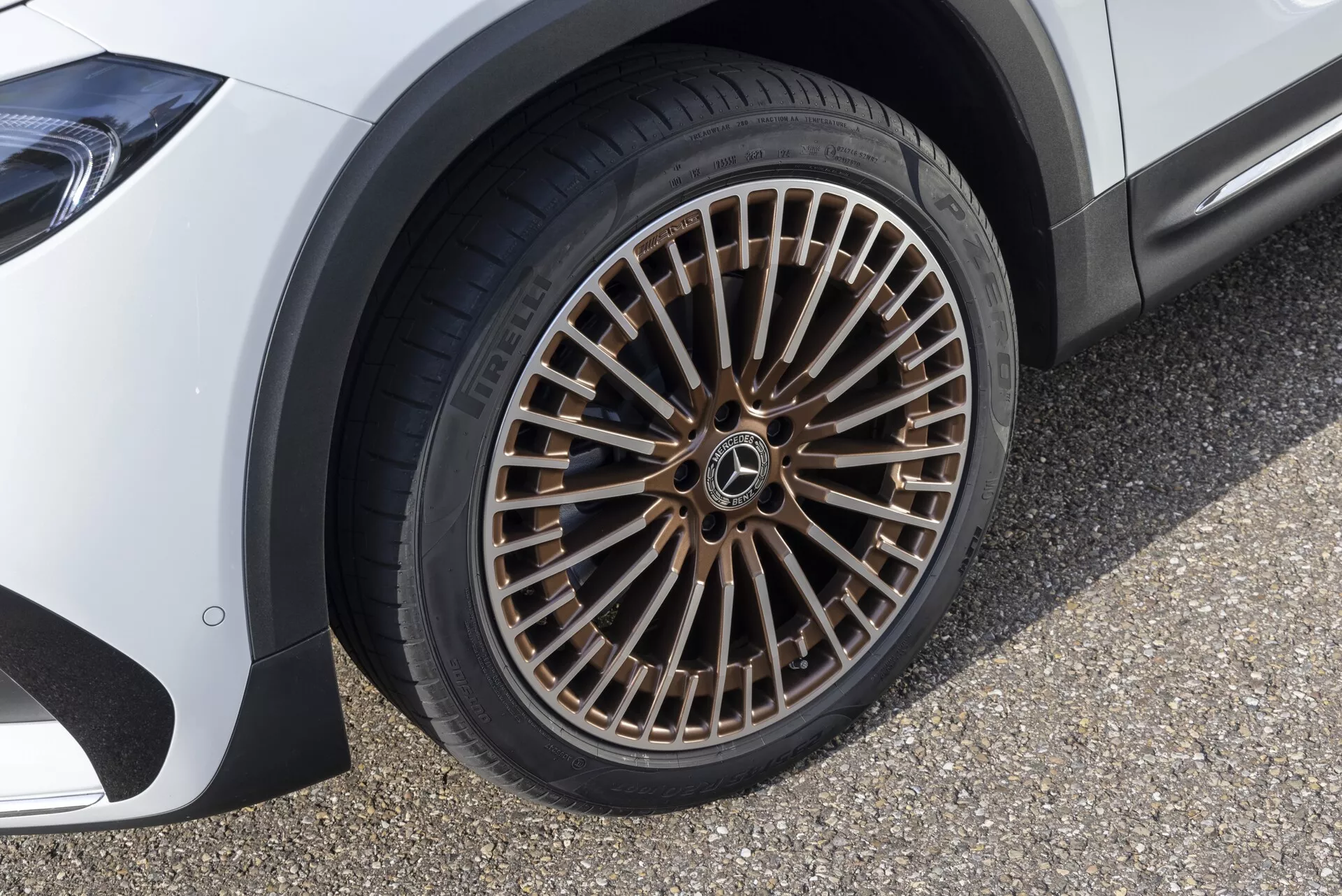 Gros plan sur la roue en alliage à multiples rayons d'une voiture de luxe vu sous un angle bas. La roue présente un grand nombre de rayons finement dessinés avec une jante métallique contrastante. Le motif de la bande de roulement du pneu est clairement visible, indiquant une utilisation régulière sur route. Le véhicule, probablement un modèle haut de gamme, est stationné sur une surface de couleur claire.