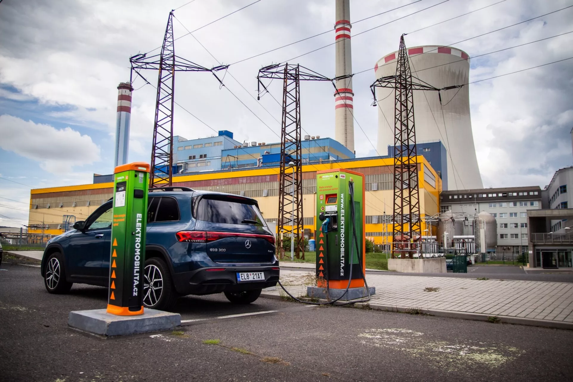Hatchback électrique Mercedes-Benz EQB de 2021 garée à une station de charge avec un câble branché, vue de trois quarts arrière, mettant en évidence ses feux arrière, fenêtre et côté passager contre un fond industriel