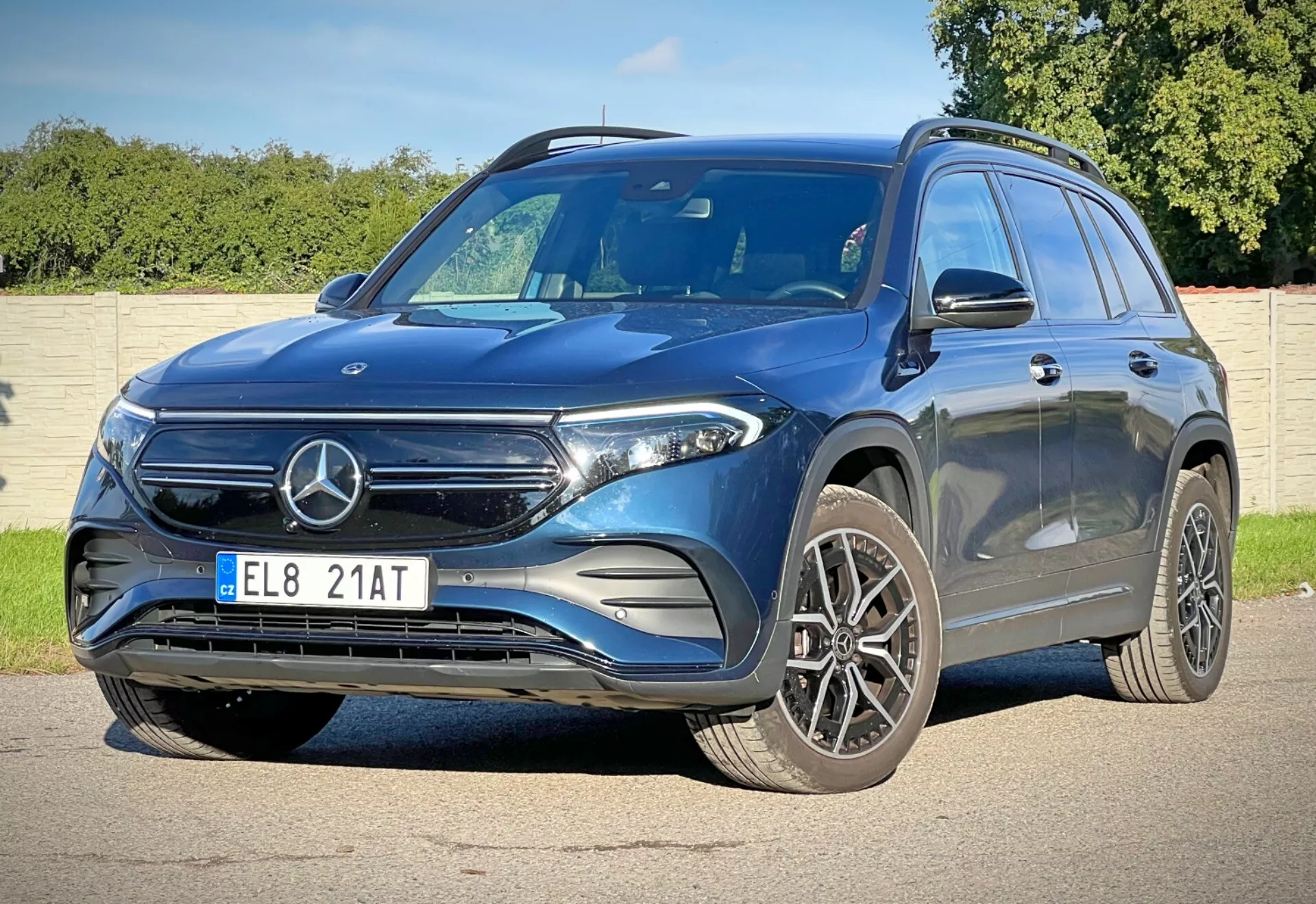 Vue avant trois quarts dynamique du Mercedes-Benz EQB 2021 montrant sa hauteur et sa posture avec des caractéristiques telles que calandre avant avec emblème, phares LED, grandes roues en alliage, pare-chocs avant sportif, capot profilé pour l'aérodynamisme, miroirs avec clignotants intégrés, une ligne de caractère pour un look dynamique, barres de toit pour une utilité ajoutée et fenêtres teintées pour la vie privée, dans une journée ensoleillée