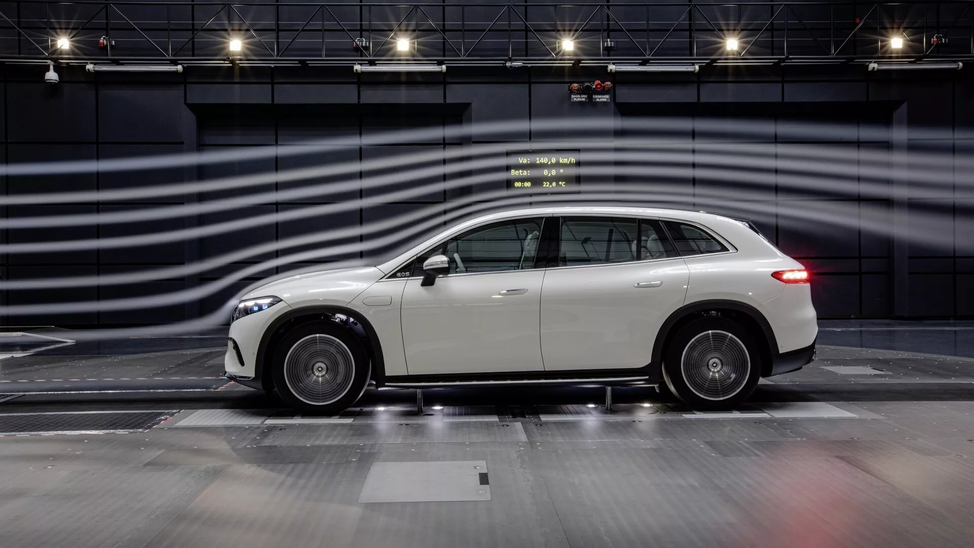 Vue de profil latéral du Mercedes EQS SUV 2022 sur une piste d'expérience, mettant en avant son design élégant, ses roues en alliage et son extérieur bien entretenu et réfléchissant. Le SUV crossover de luxe moderne présente un toit légèrement incliné vers l'arrière, suggérant une esthétique sportive combinée à la praticité d'un SUV. La photo capture toute la longueur de la voiture avec des lignes floues en arrière-plan simulant une grande vitesse, mettant en valeur le design et les performances implicites du véhicule dans un environnement contrôlé et monochromatique.