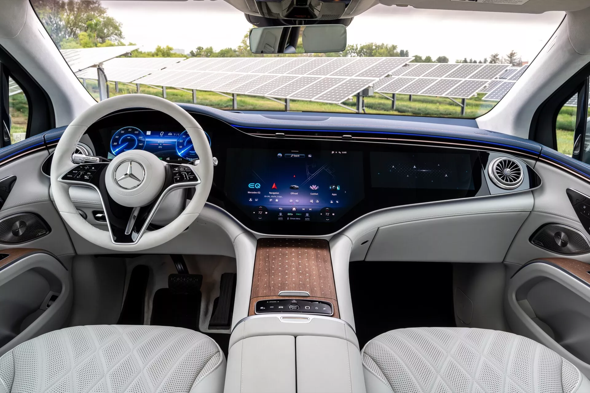 Intérieur du Mercedes EQS-SUV 2022, présentant une rangée avant luxueuse avec un volant à deux branches, des commandes tactiles intégrées, un tableau de bord entièrement numérique, un écran tactile central expansif couvrant le tableau de bord, des commandes physiques minimales pour le climat, une aération continue, des sièges en cuir blanc matelassé, des finitions en bois et une console centrale avec touchpad et rangement.