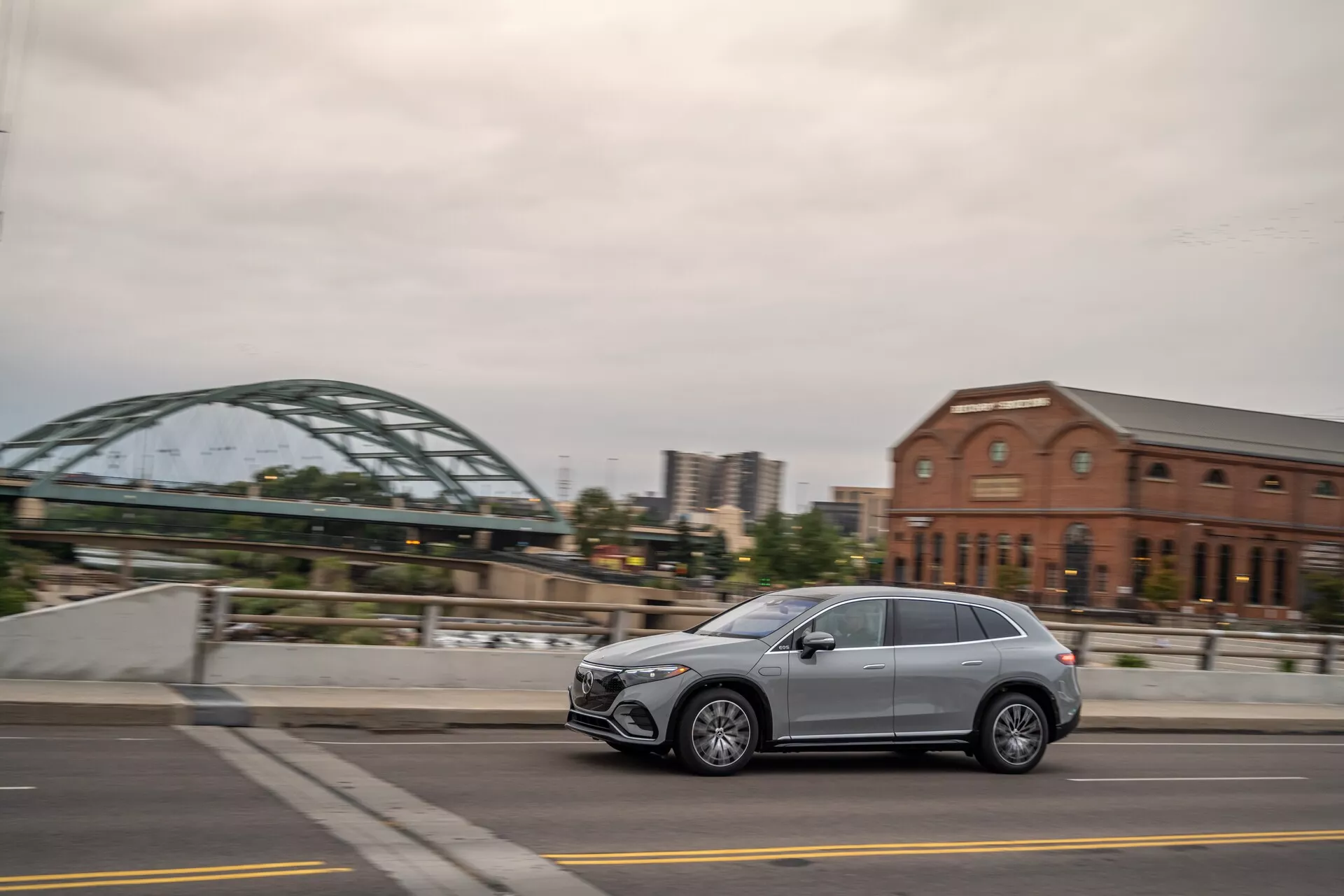 Vue de profil latéral d'un Mercedes EQS-SUV 2022 moderne roulant dans une rue de la ville, montrant un design élégant, cinq portes, des roues en alliage et des phares à LED. Capturé sous un angle légèrement arrière avec un arrière-plan flou.
